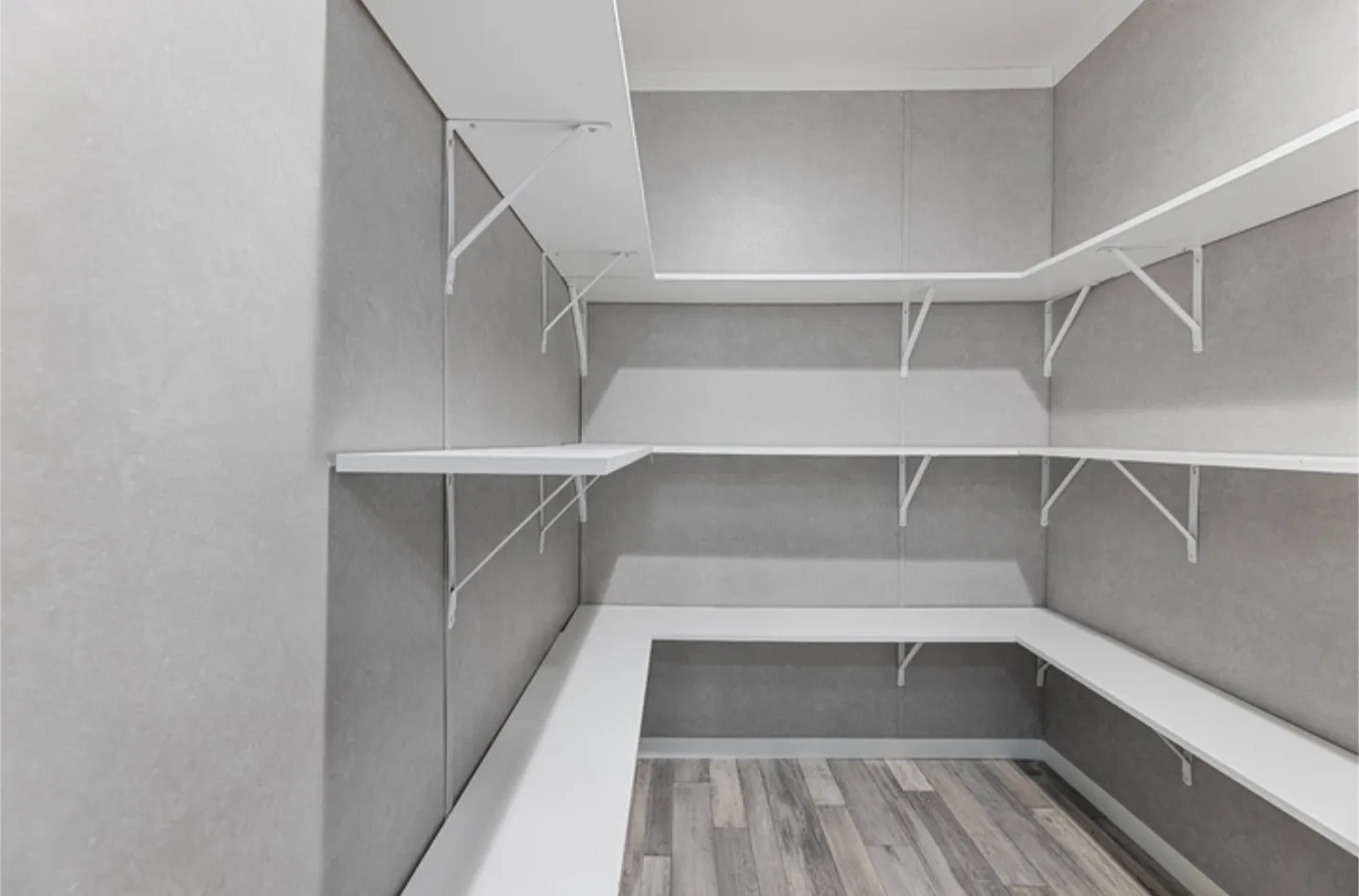 Built-in shelving with white brackets, gray panel walls, white baseboards, and wood-finish flooring