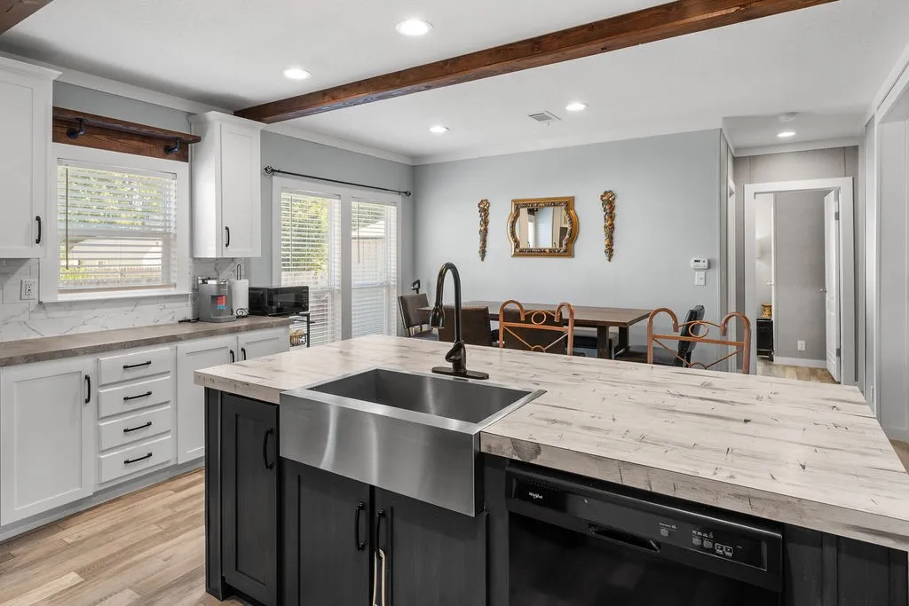 Kitchen island with a farmhouse sink, white perimeter cabinetry, wood-finish flooring, and exposed ceiling beams