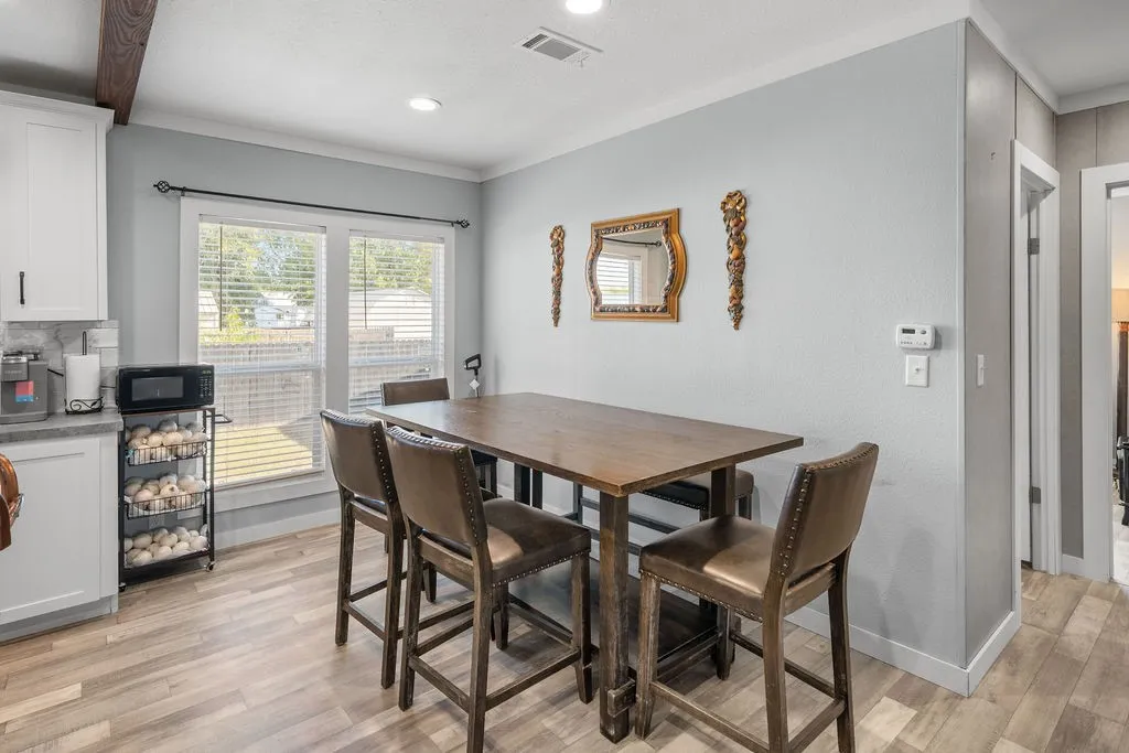 Light-colored wood-finish flooring, white cabinetry with dark hardware, recessed ceiling lighting, and a large window with horizontal blinds