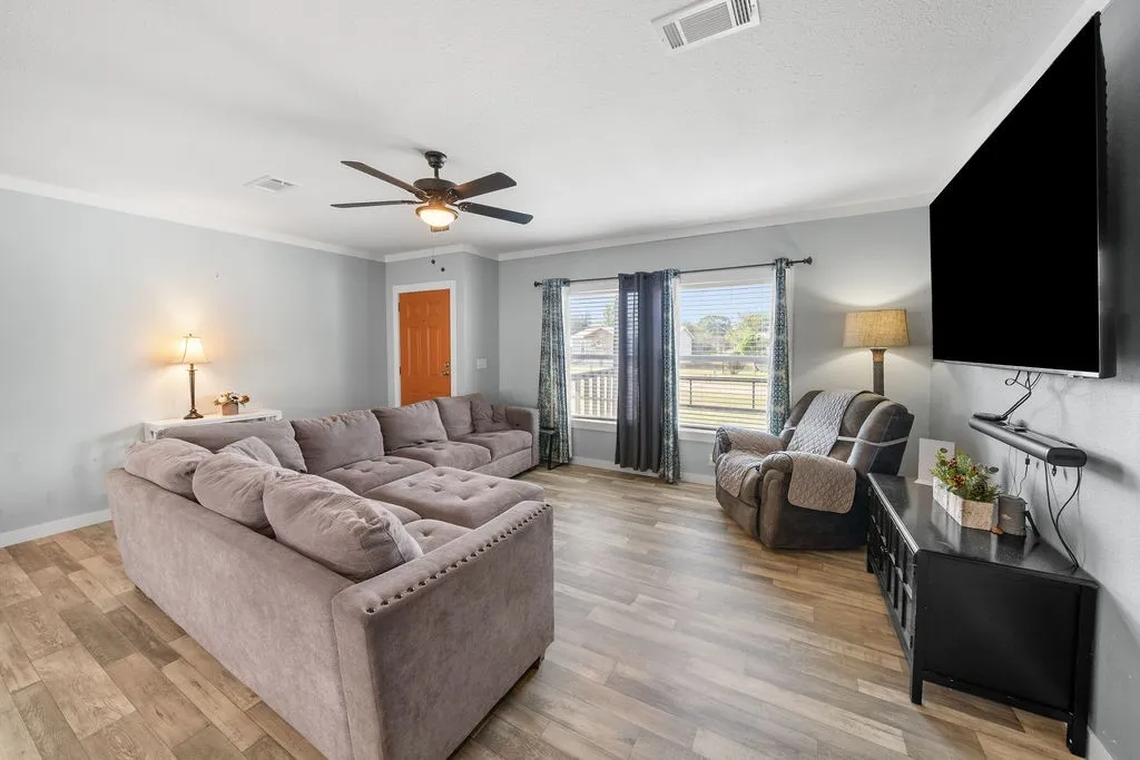 Wood-finish flooring throughout, ceiling fan with integrated lighting, multiple windows providing natural light, crown molding, and a solid-core entry door