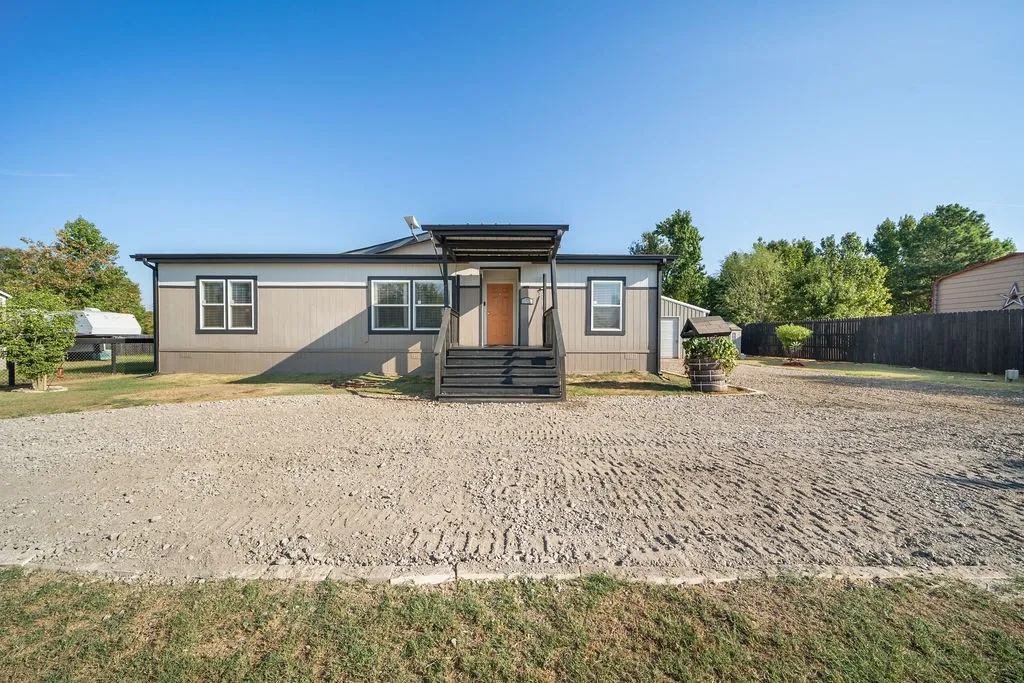 Two-tone exterior with dark trim, covered porch entry, and gravel driveway