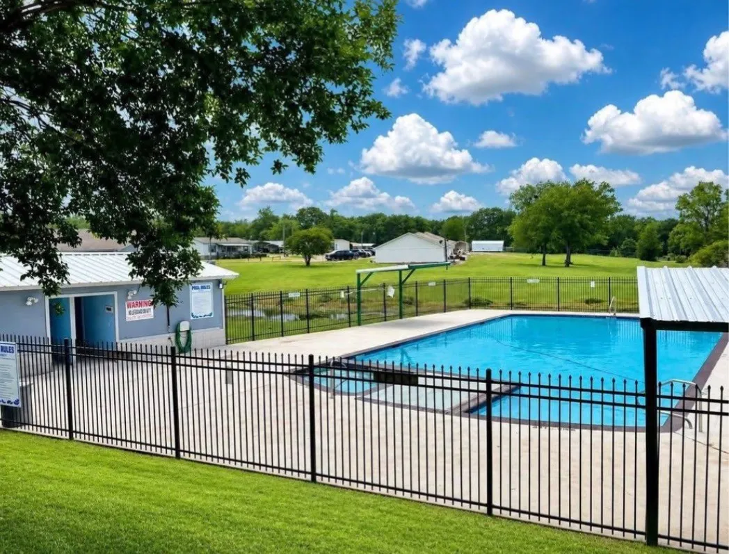 Fenced swimming pool with concrete decking, adjacent pool house, and surrounding green space
