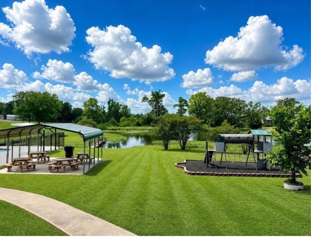 Expansive green lawn with a water feature, covered picnic area, and a playset with a wood chip base