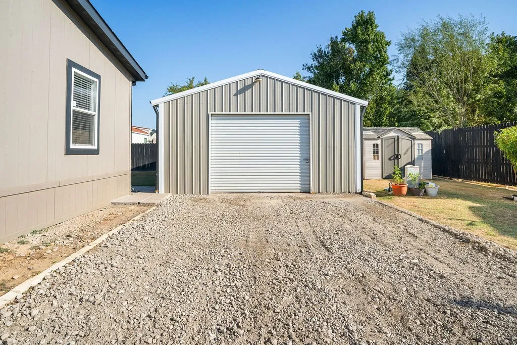 Detached metal garage with a roll-up door, gravel driveway, and a separate storage shed in the backyard