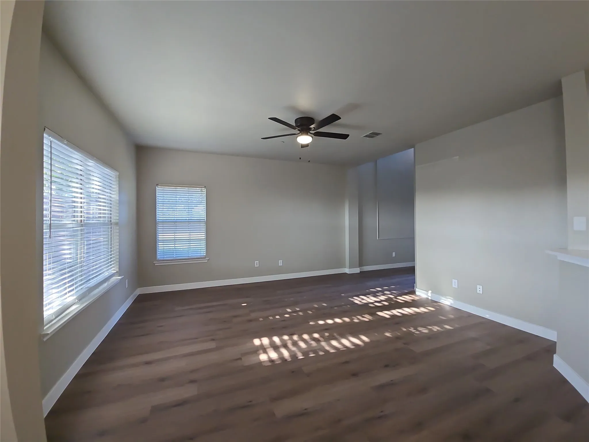 Spacious room featuring wood-finish flooring, multiple windows with blinds, a ceiling fan with integrated lighting, and neutral wall tones