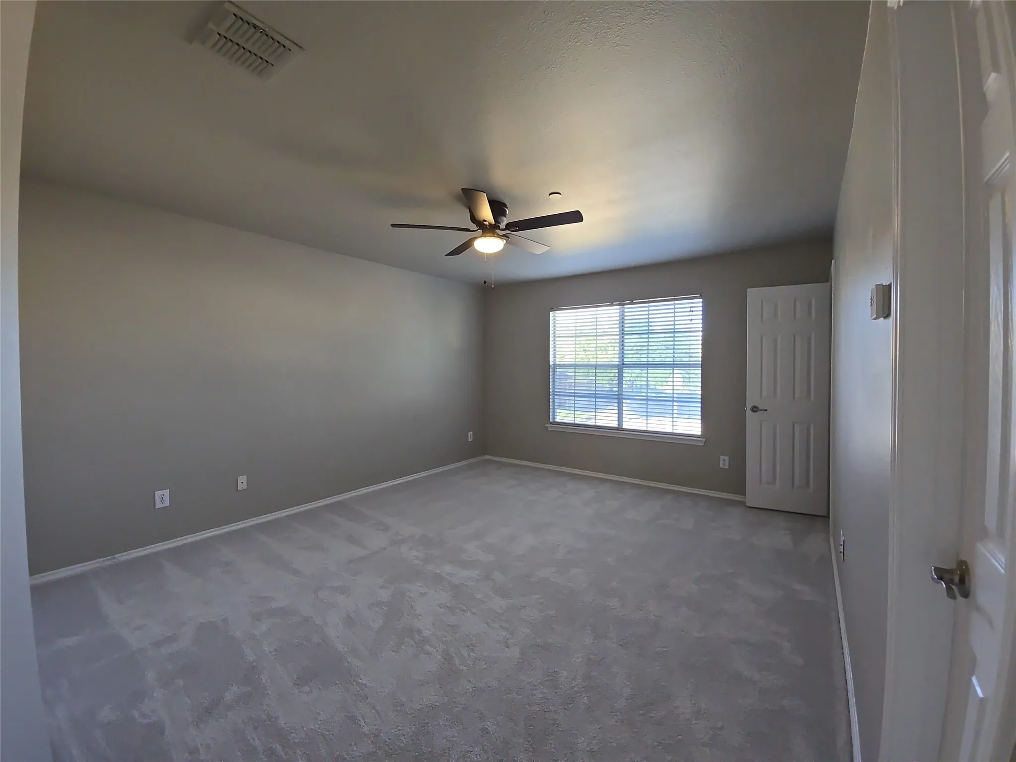 Expansive room featuring light gray carpeting, neutral-toned walls, and a large window with blinds