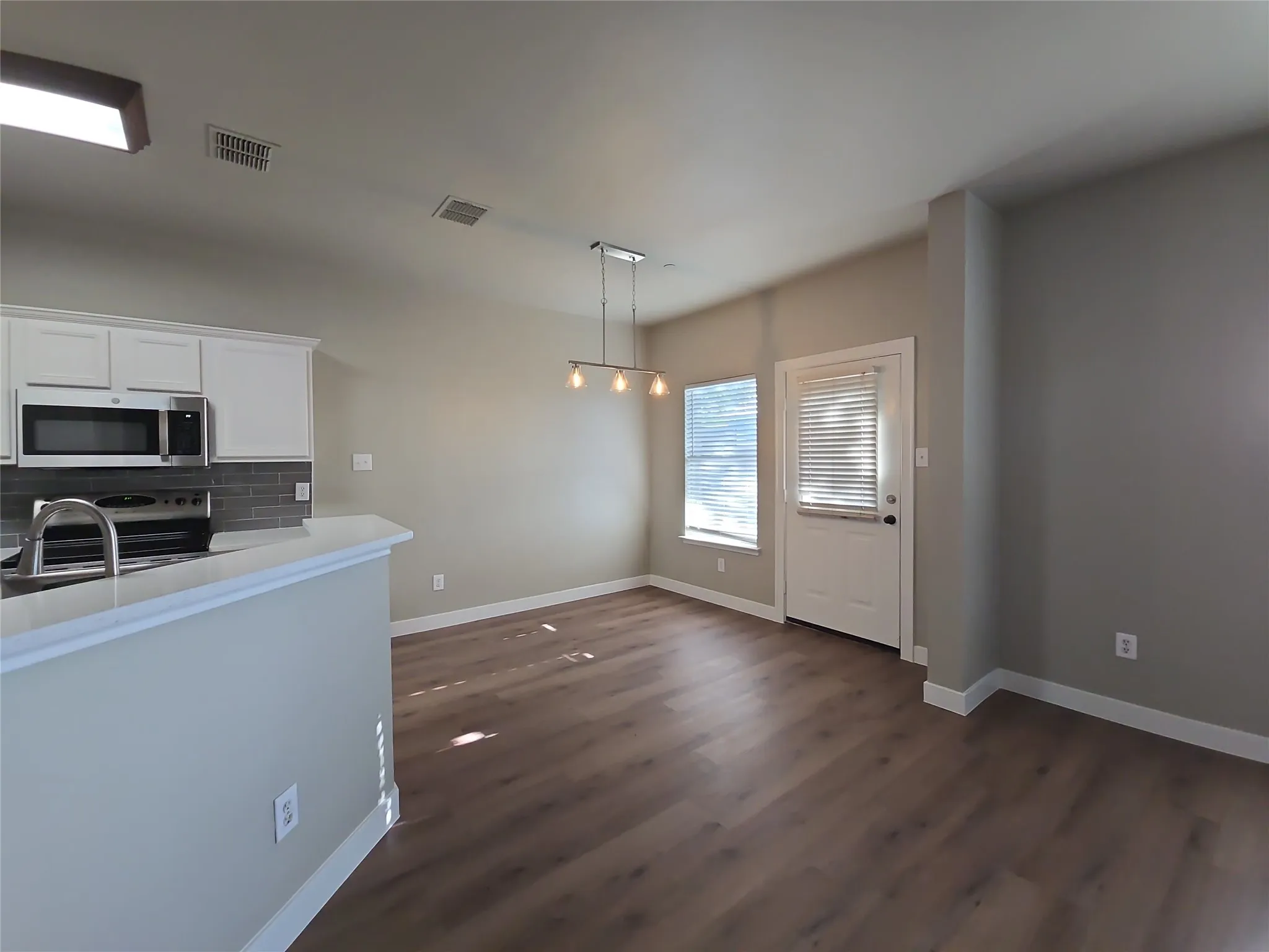 White shaker cabinetry, stainless steel appliances, grey subway tile backsplash, wood-finish flooring, and a contemporary chandelier
