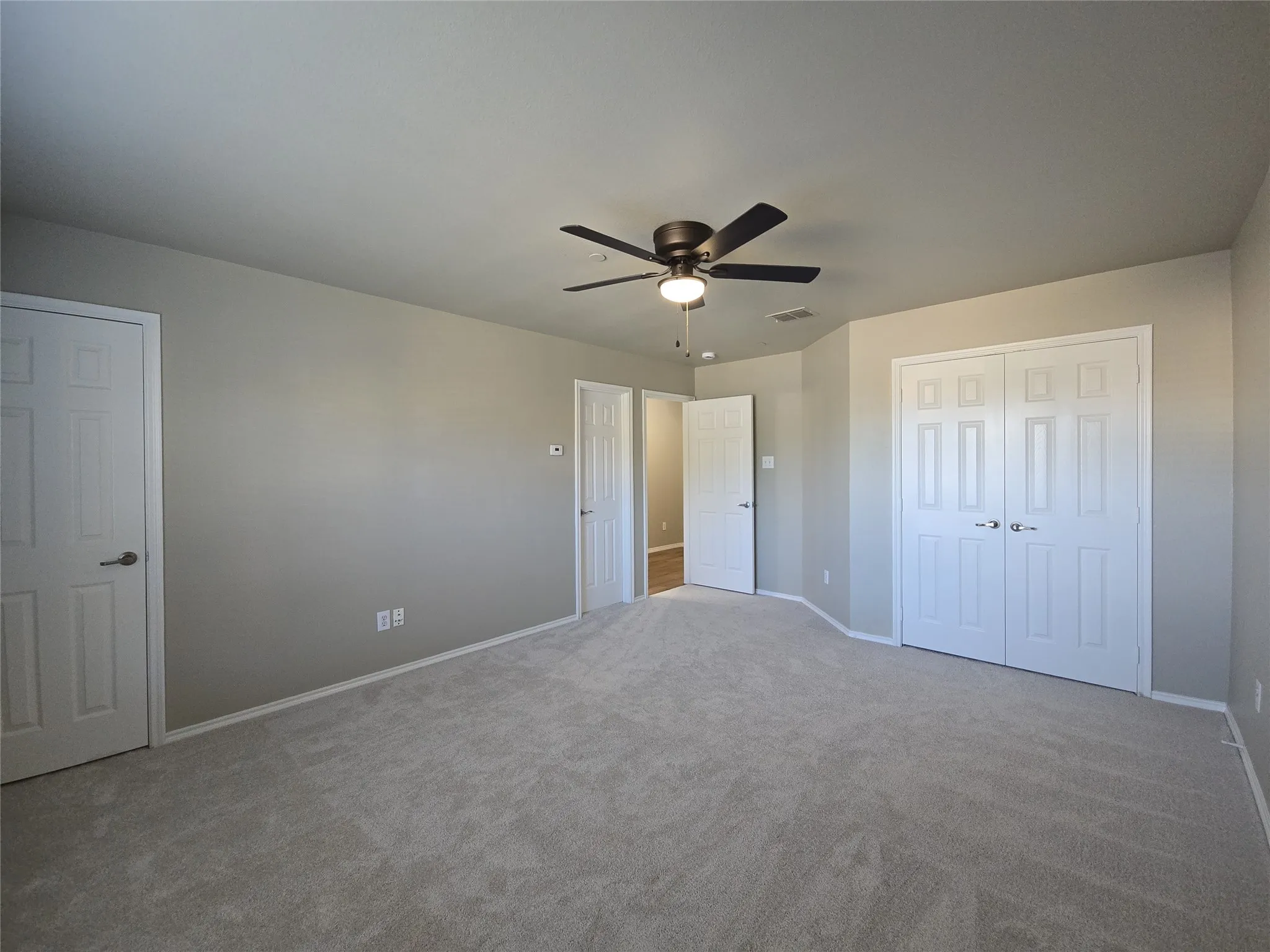 Neutral-toned wall paint, light-colored carpeting, multiple paneled doors, and a ceiling fan with integrated lighting