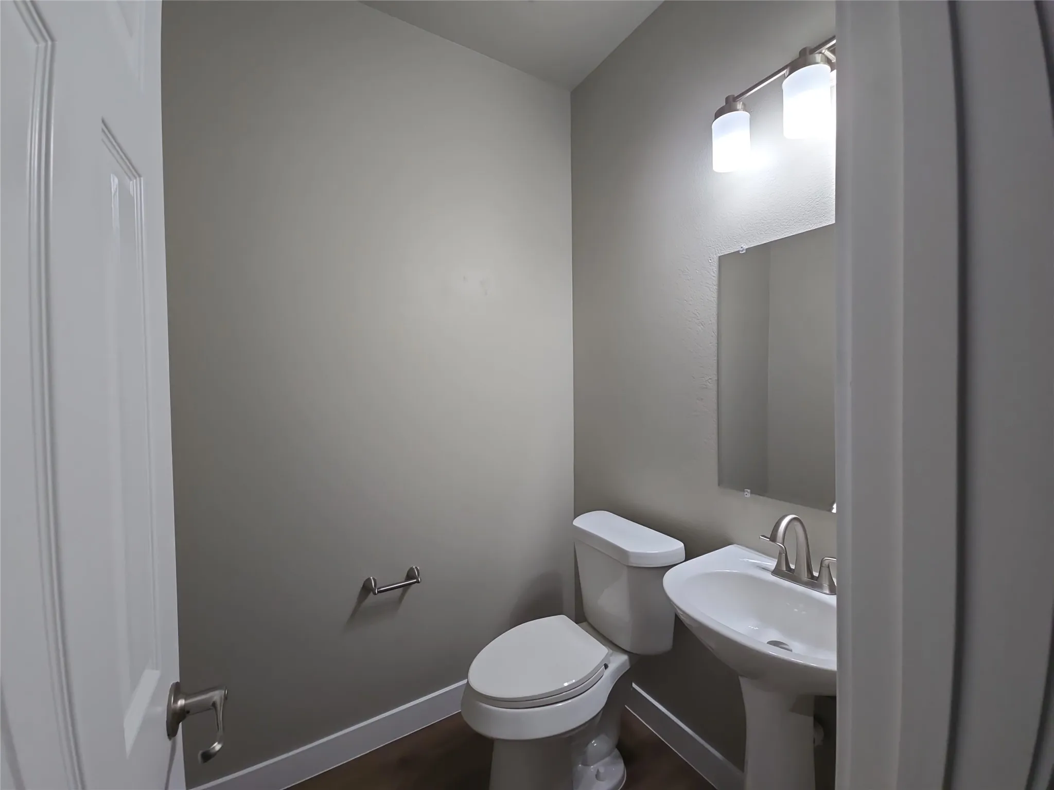 Pedestal sink with a brushed nickel faucet, wall-mounted mirror, and overhead vanity lighting
