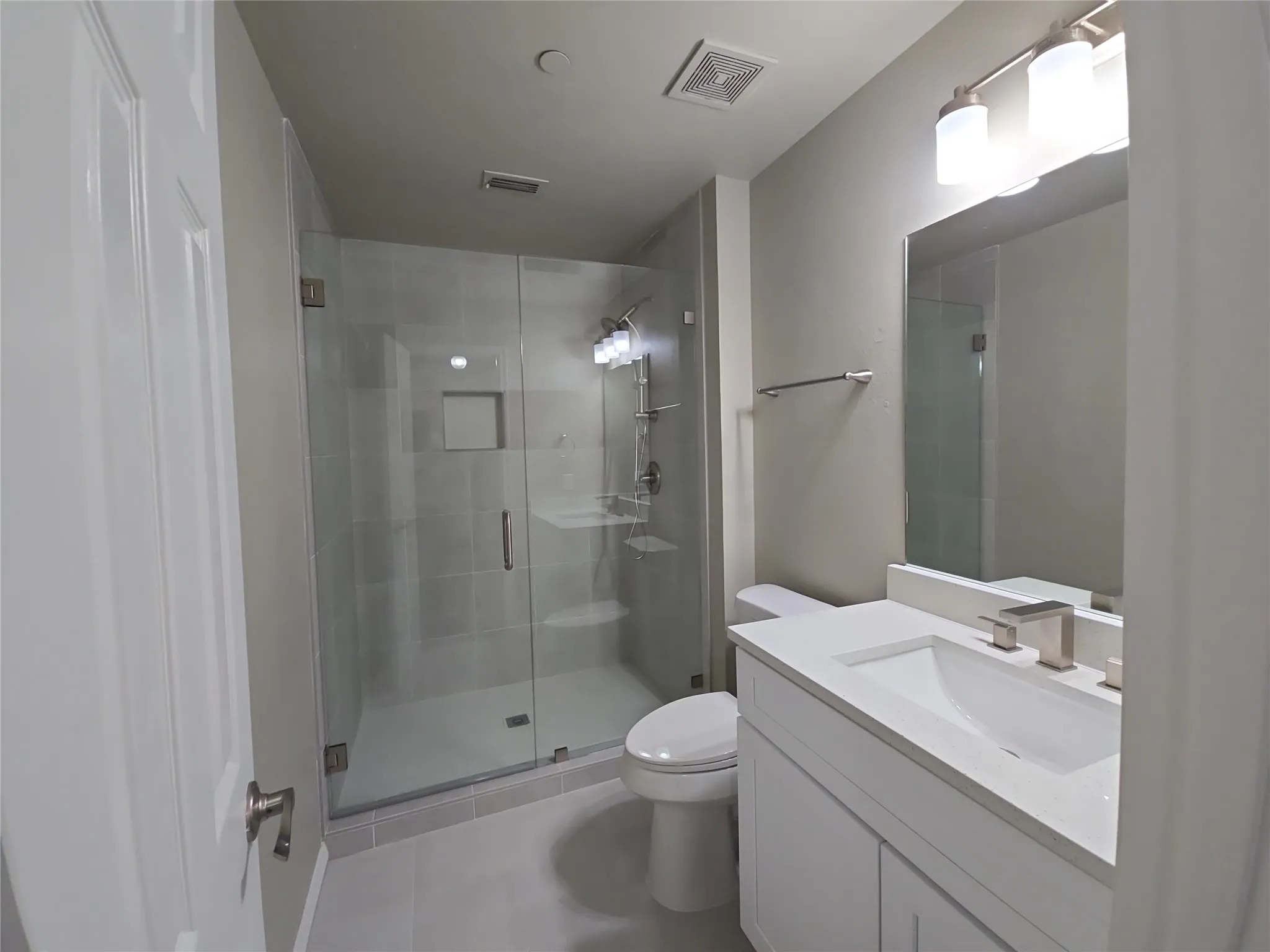 Glass-enclosed shower with a recessed shelf, white vanity with an integrated sink, brushed nickel faucet, and a wall-mounted mirror