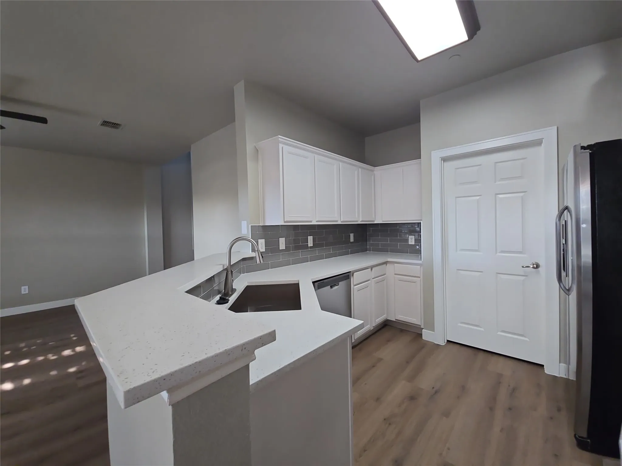White cabinetry, solid surface countertops, stainless steel appliances, subway tile backsplash, and wood-finish flooring