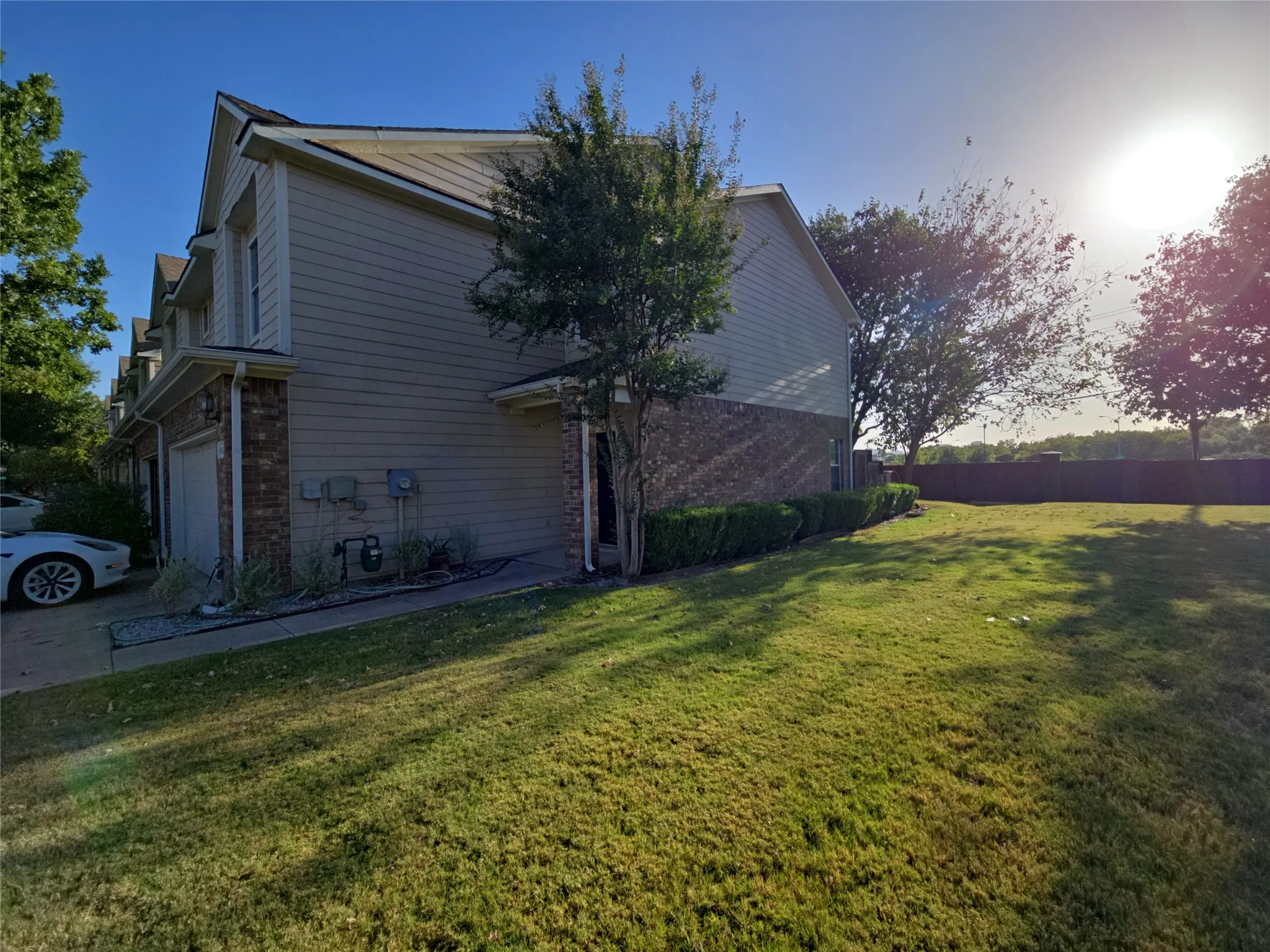 Two-story townhouse featuring a brick and siding exterior, an attached garage, and a lush lawn bordered by mature landscaping