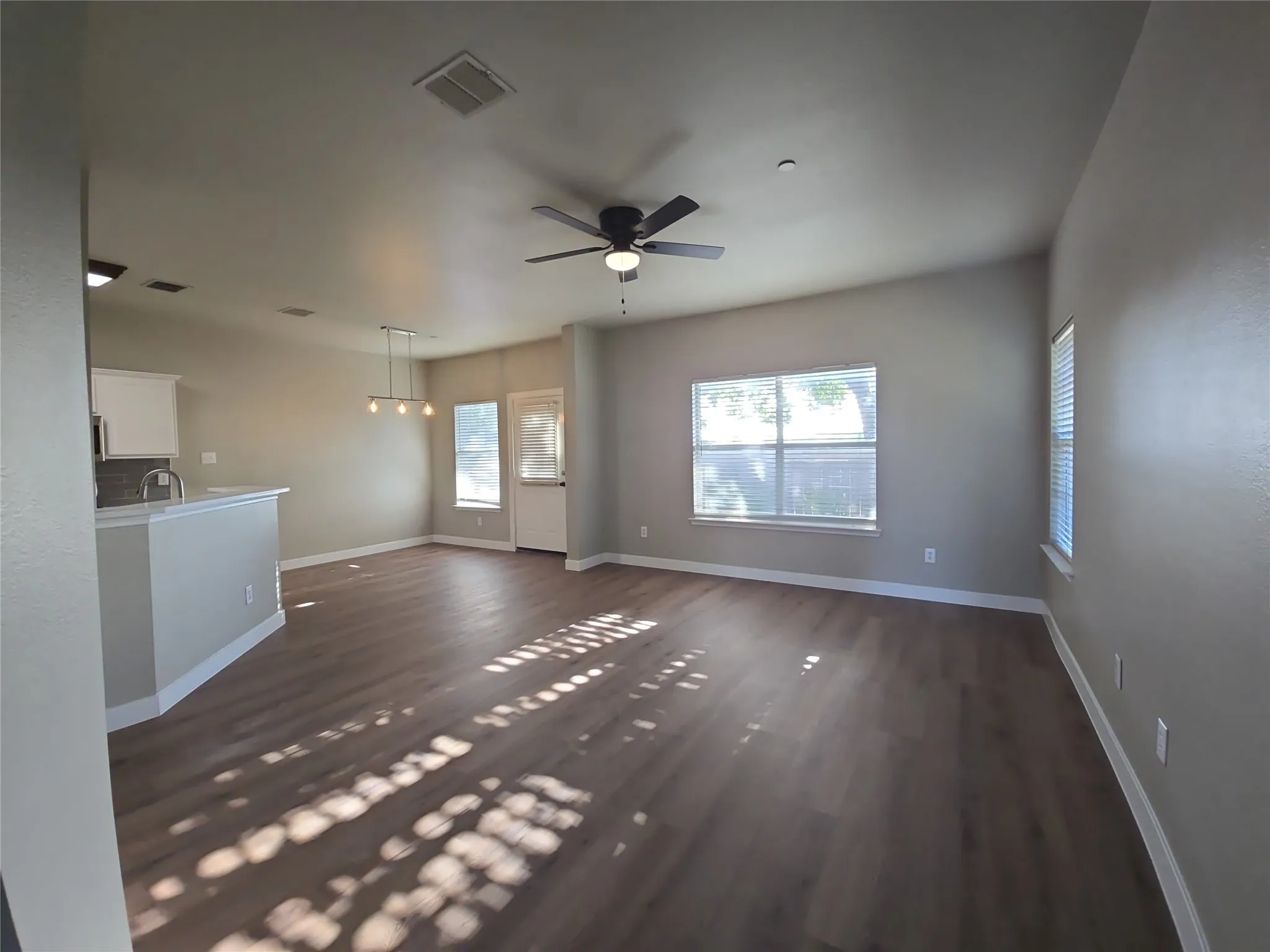 Wood-finish flooring throughout, vaulted ceiling with a ceiling fan, and multiple windows with blinds