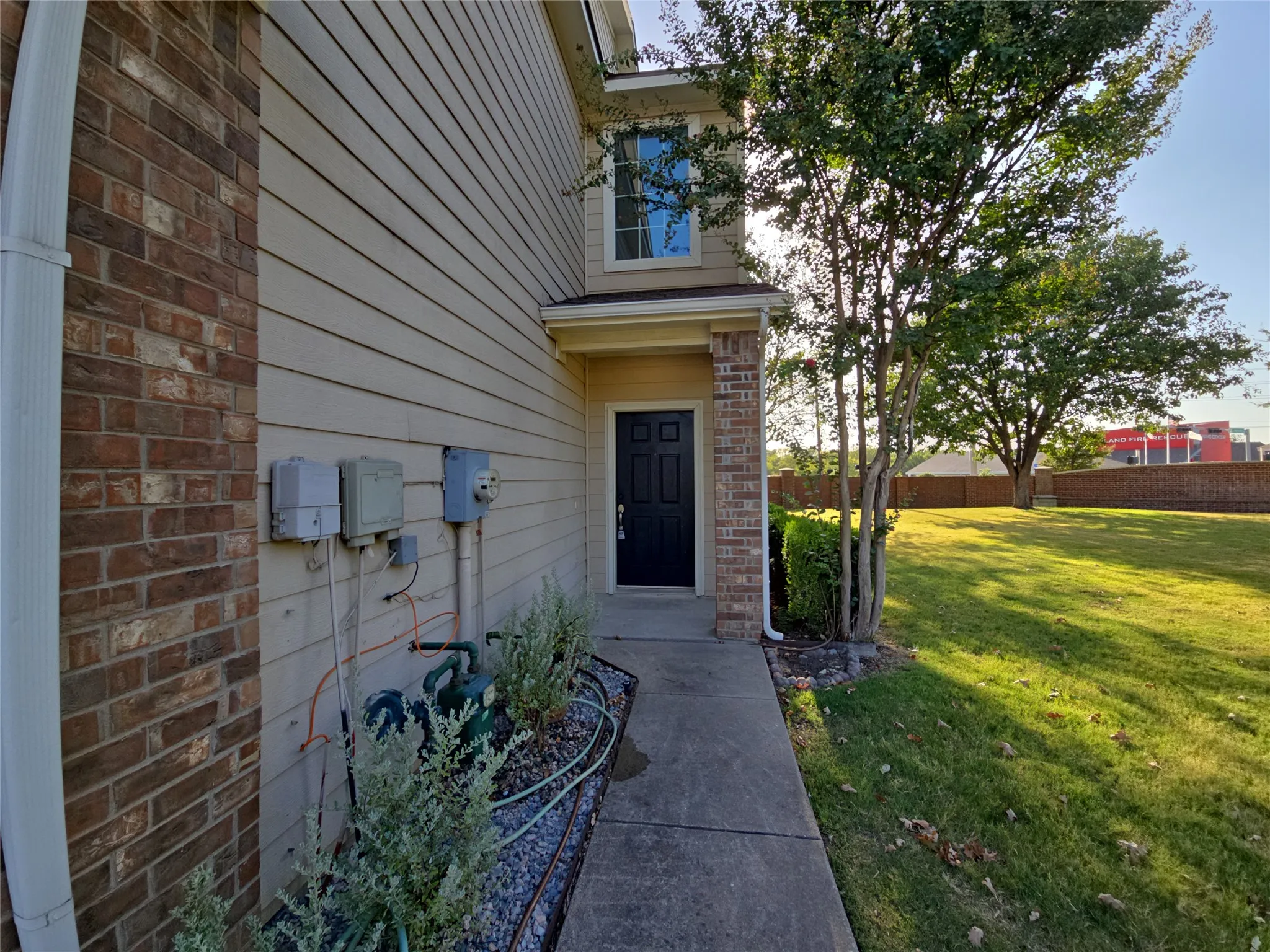 Siding exterior with brick accents, concrete walkway, and a landscaped bed with gravel and plantings