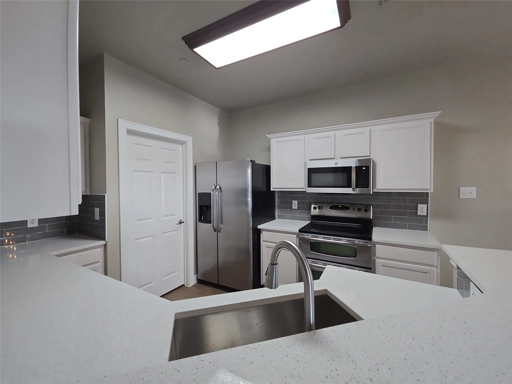 White cabinetry, stainless steel appliances, grey subway tile backsplash, white countertops, and an undermount sink with a gooseneck faucet