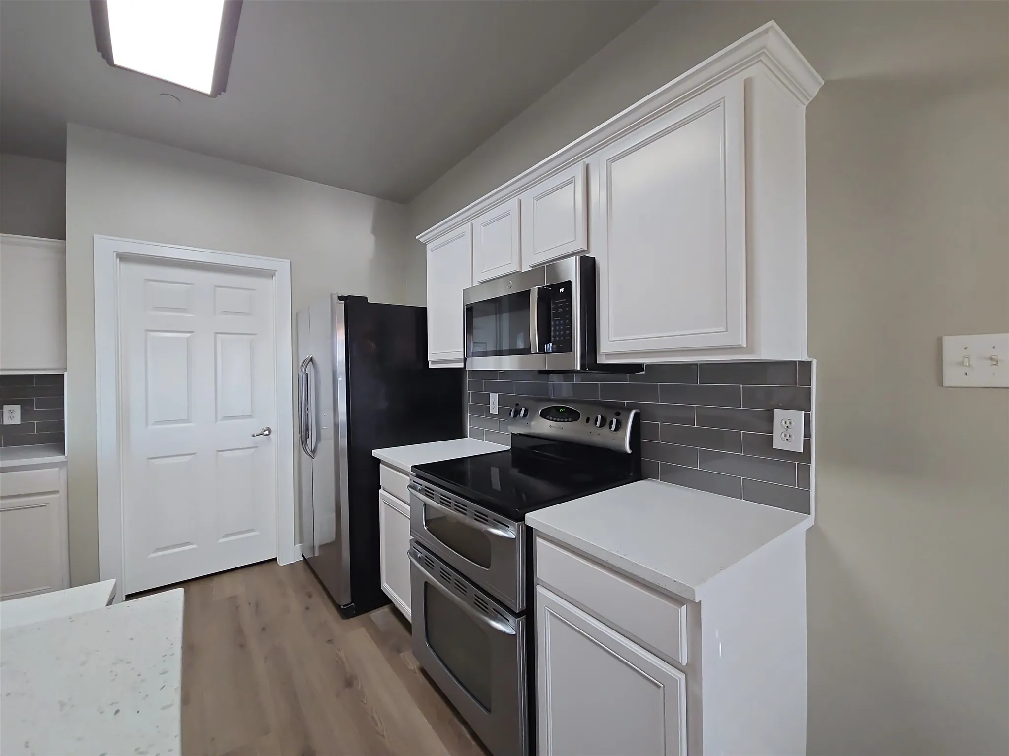 White shaker-style cabinetry with crown molding, stainless steel appliances, wood-finish flooring, white countertops, and a gray subway tile backsplash