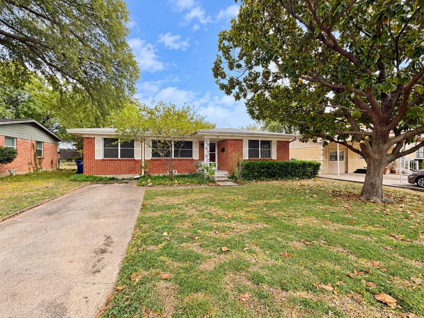 Brick exterior with white shutters, mature trees, and a concrete driveway