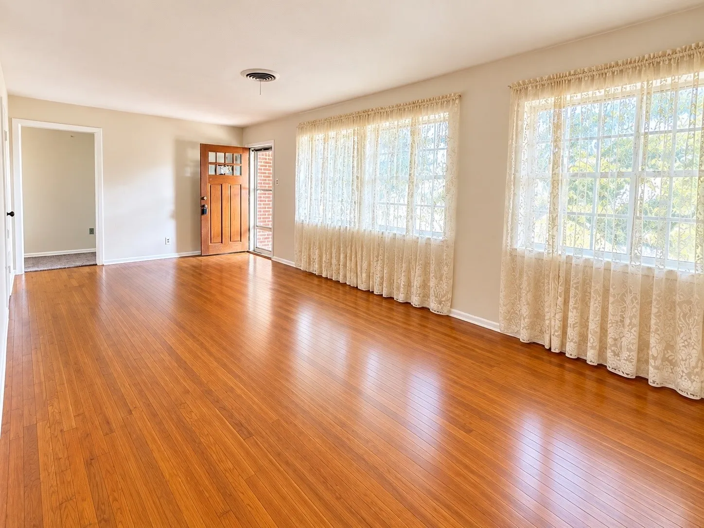 Warm wood-finish flooring, multiple window openings, and a solid wood entry door