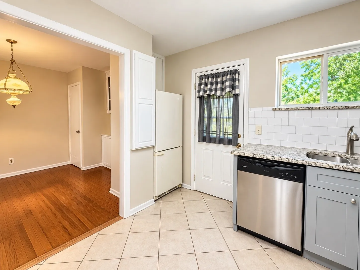 Kitchen featuring stainless steel dishwasher, white subway tile backsplash, granite-style countertop, and gray cabinetry