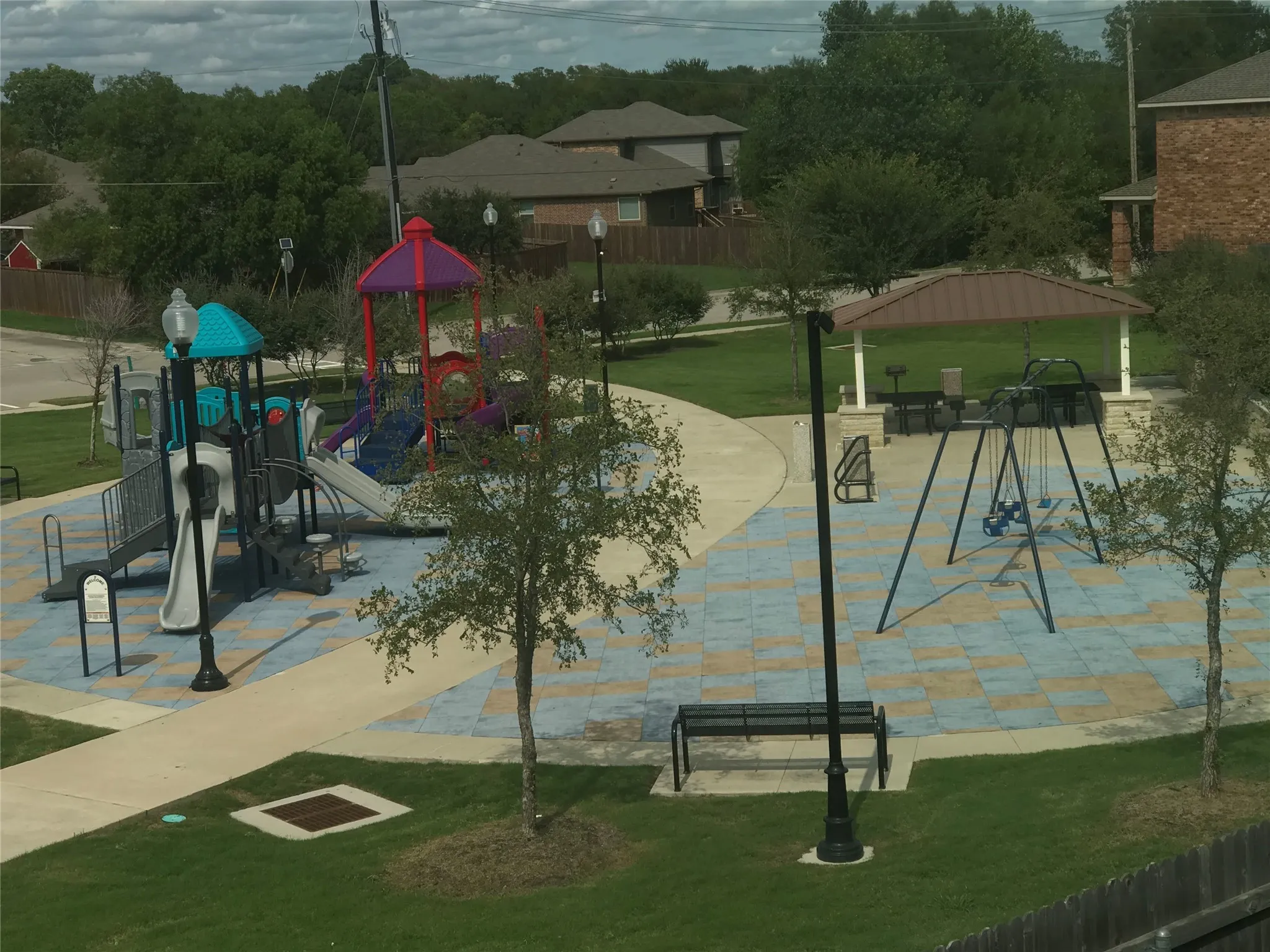 Community park featuring a multi-level playground, swing set, covered picnic area, and paved walking paths