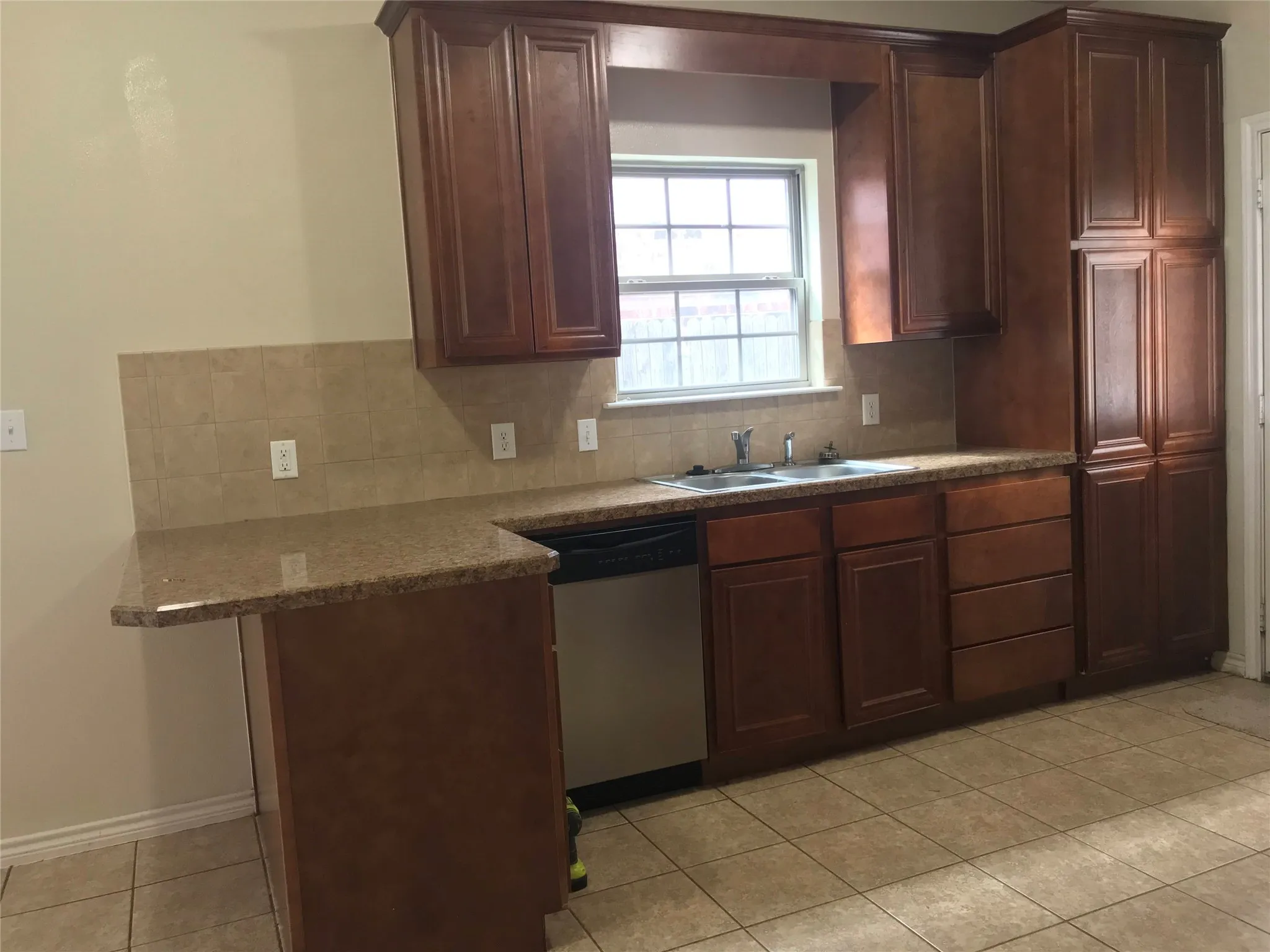 Wood-finish cabinetry and built-in pantry storage, granite-finish countertops, tile backsplash, and tile flooring