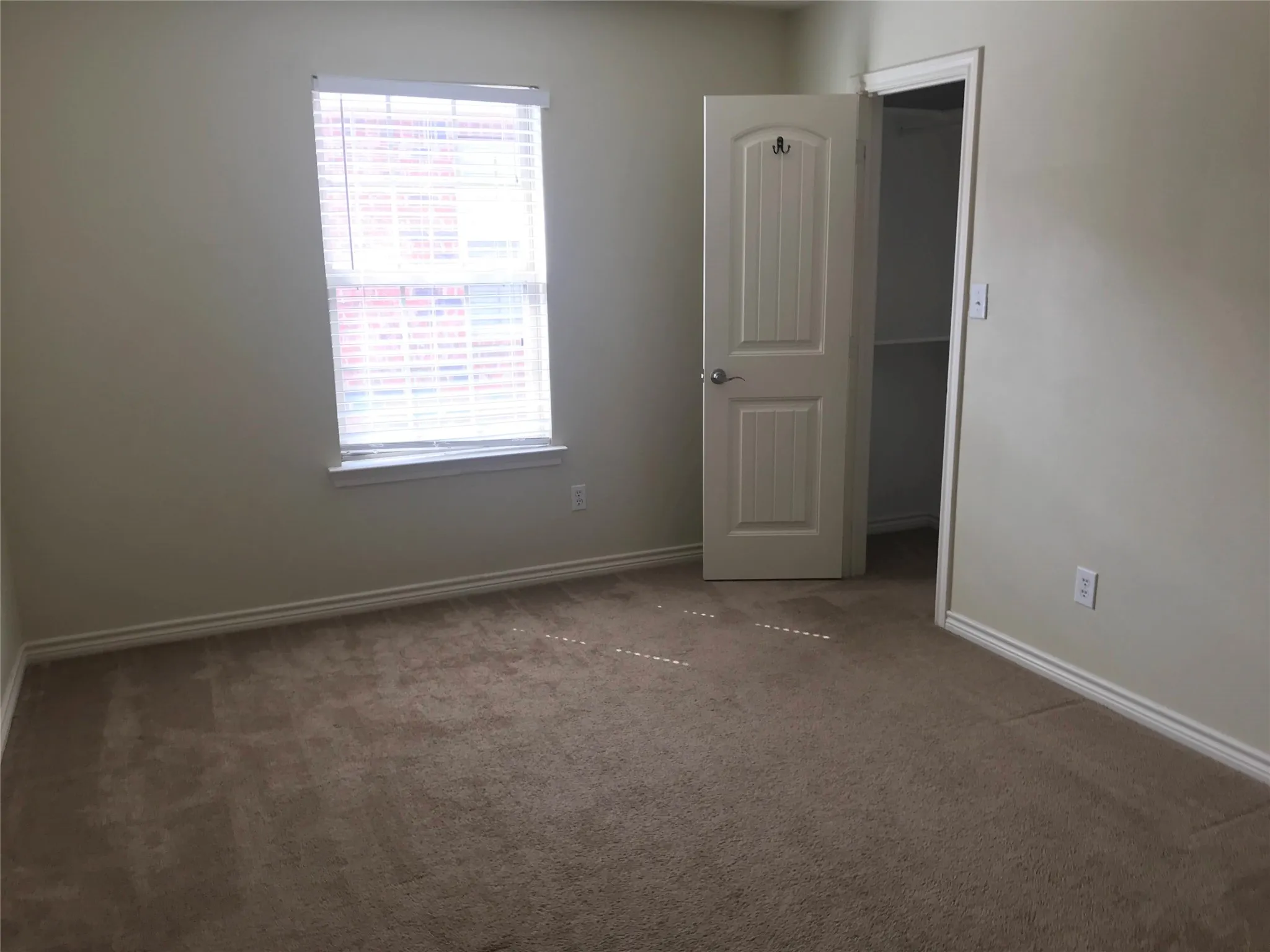 Neutral tone wall paint, carpeted flooring, window with blinds, paneled door, and closet with shelving