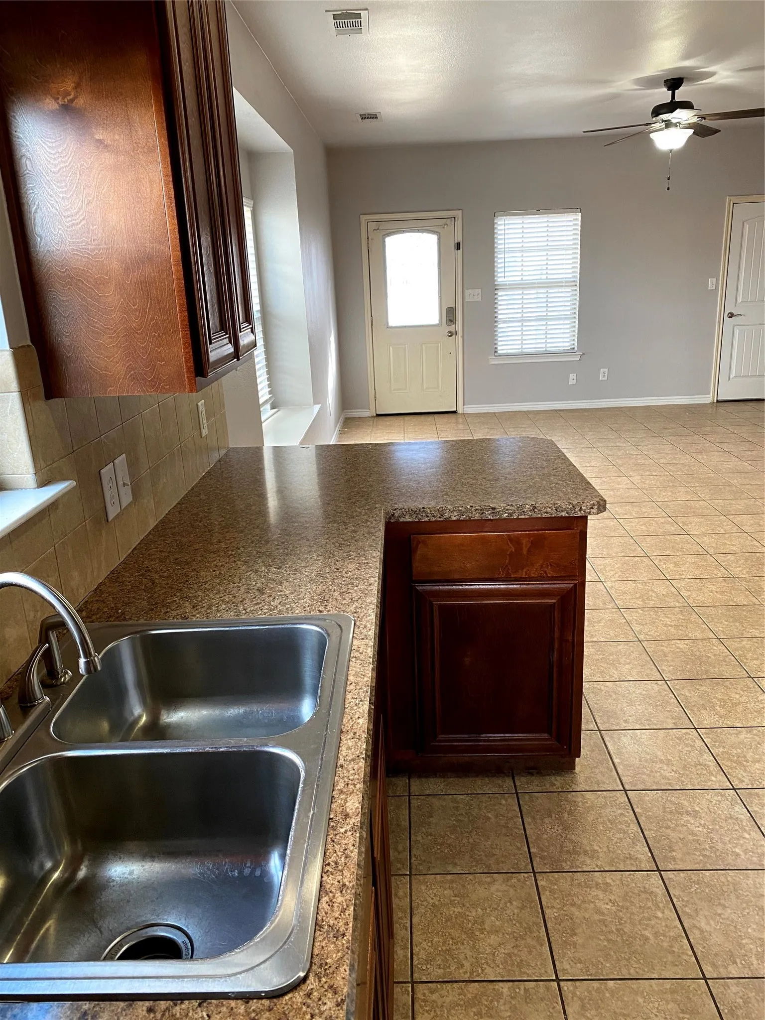 Kitchen featuring a double basin stainless steel sink, dark wood-finish cabinetry, and a peninsula with a stone-finish countertop