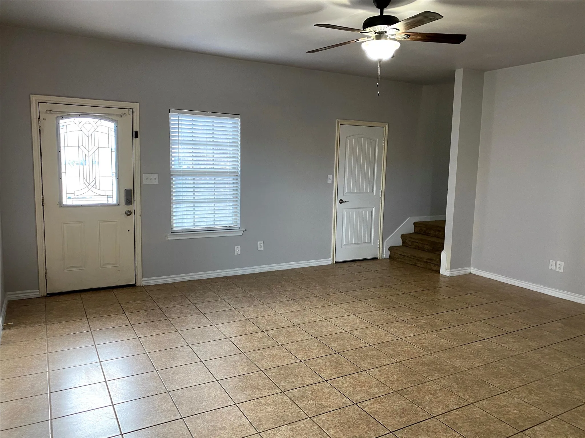 Spacious interior featuring tile flooring, a decorative glass-paneled front door, window with blinds, and a ceiling fan with integrated lighting