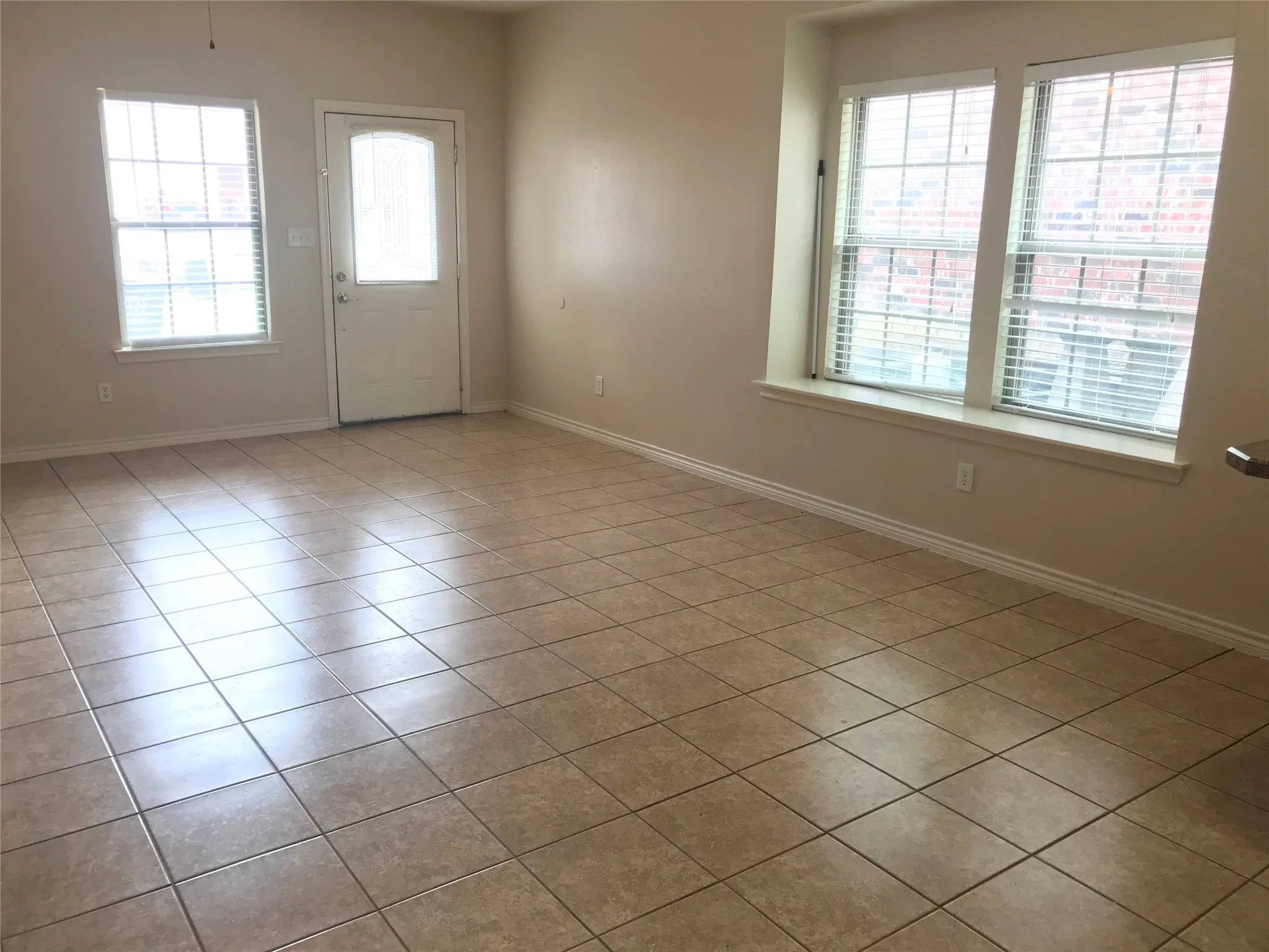 Rectangular floor tiles, multiple windows with blinds, and a door with an arched glass insert