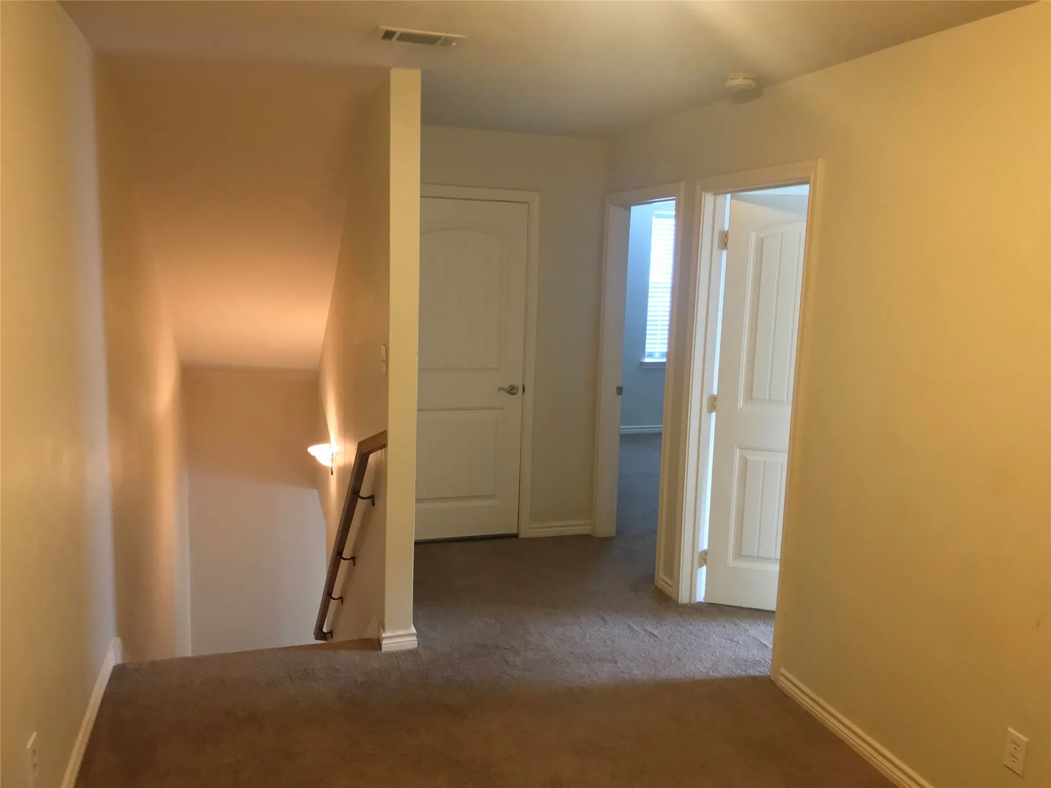 Upper-level landing with carpet flooring, a wall-mounted light fixture, and two panel doors