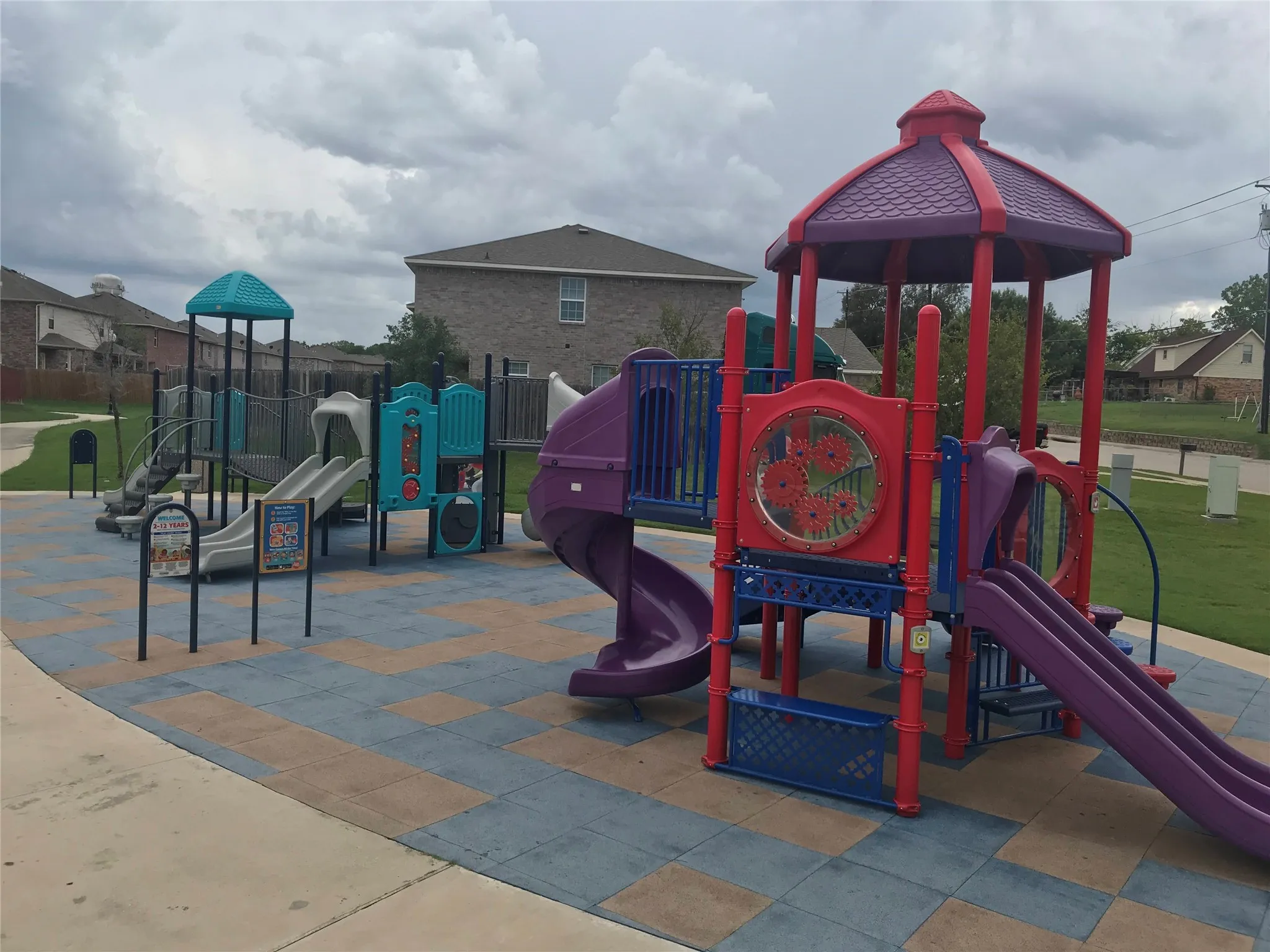 Community playground featuring multiple slides and various play structures set on a multi-colored soft-fall surface