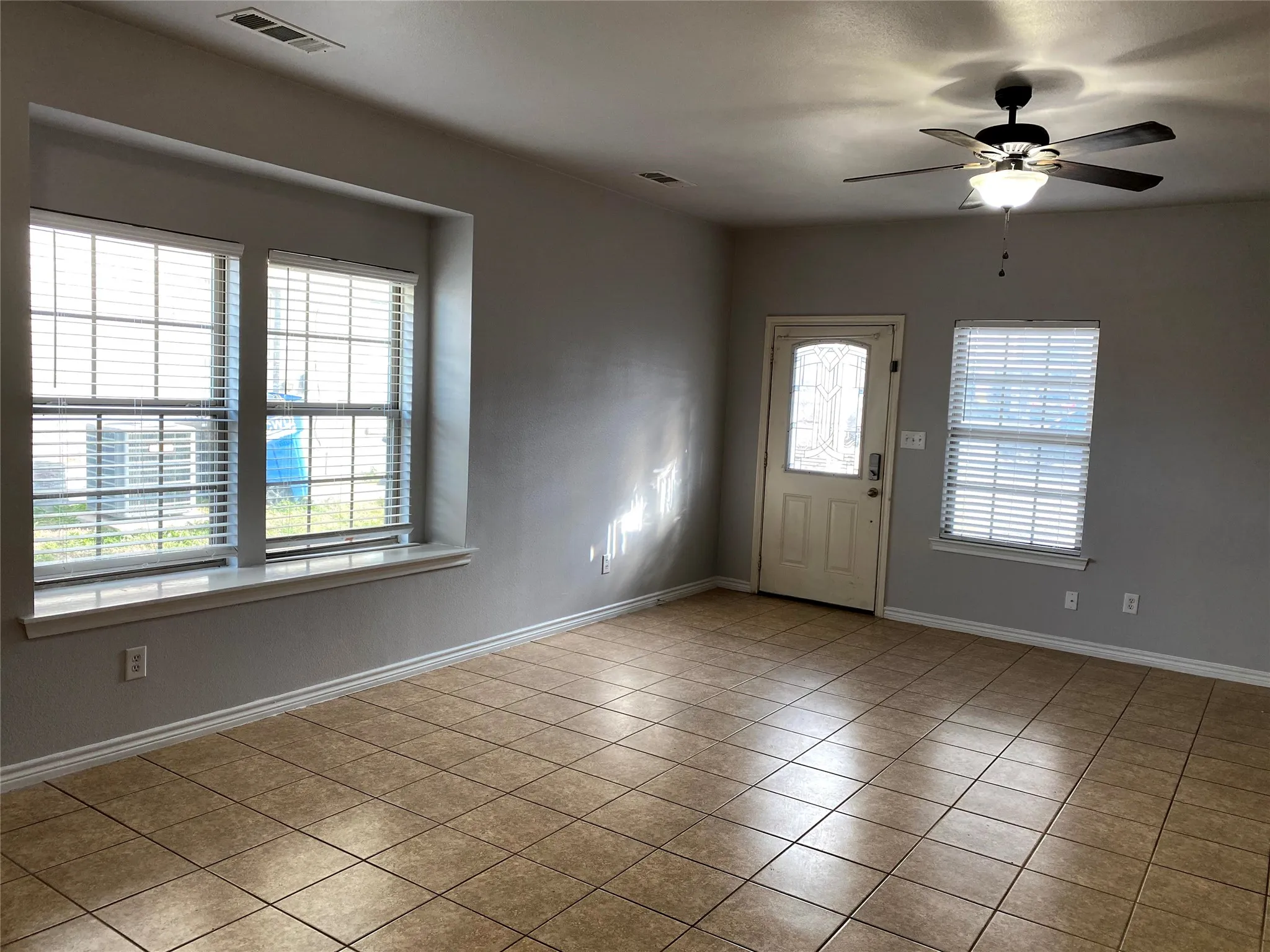Tiled flooring, multiple windows with blinds, ceiling fan with integrated lighting, and a front entry door with decorative glass