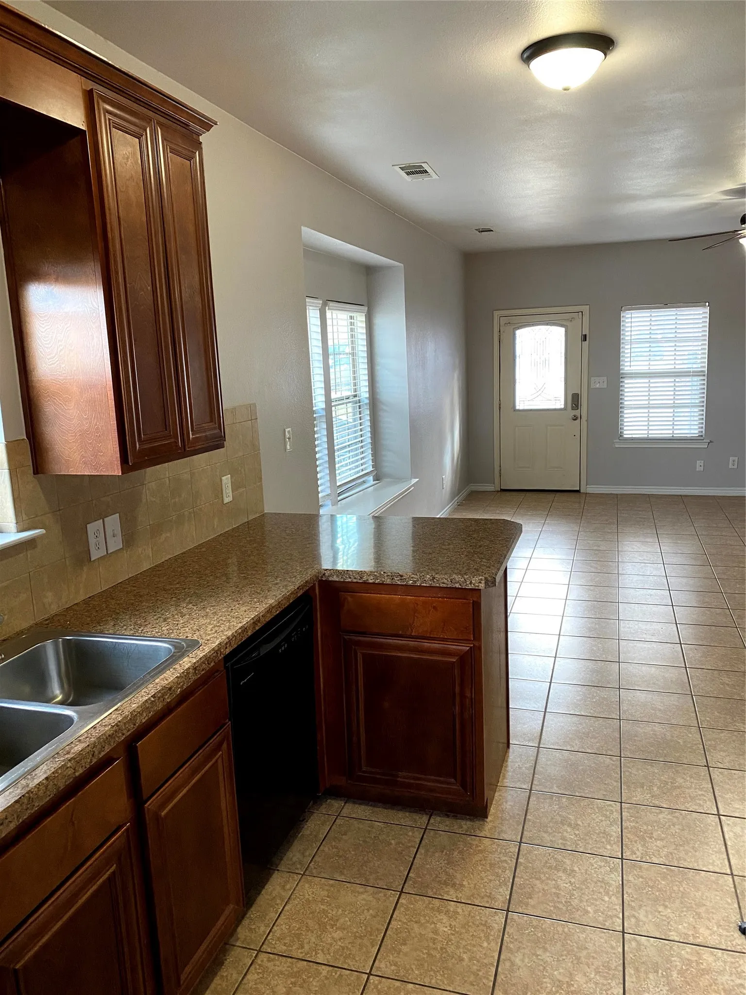 Kitchen featuring wood-finish cabinetry, a double basin sink, and a black dishwasher