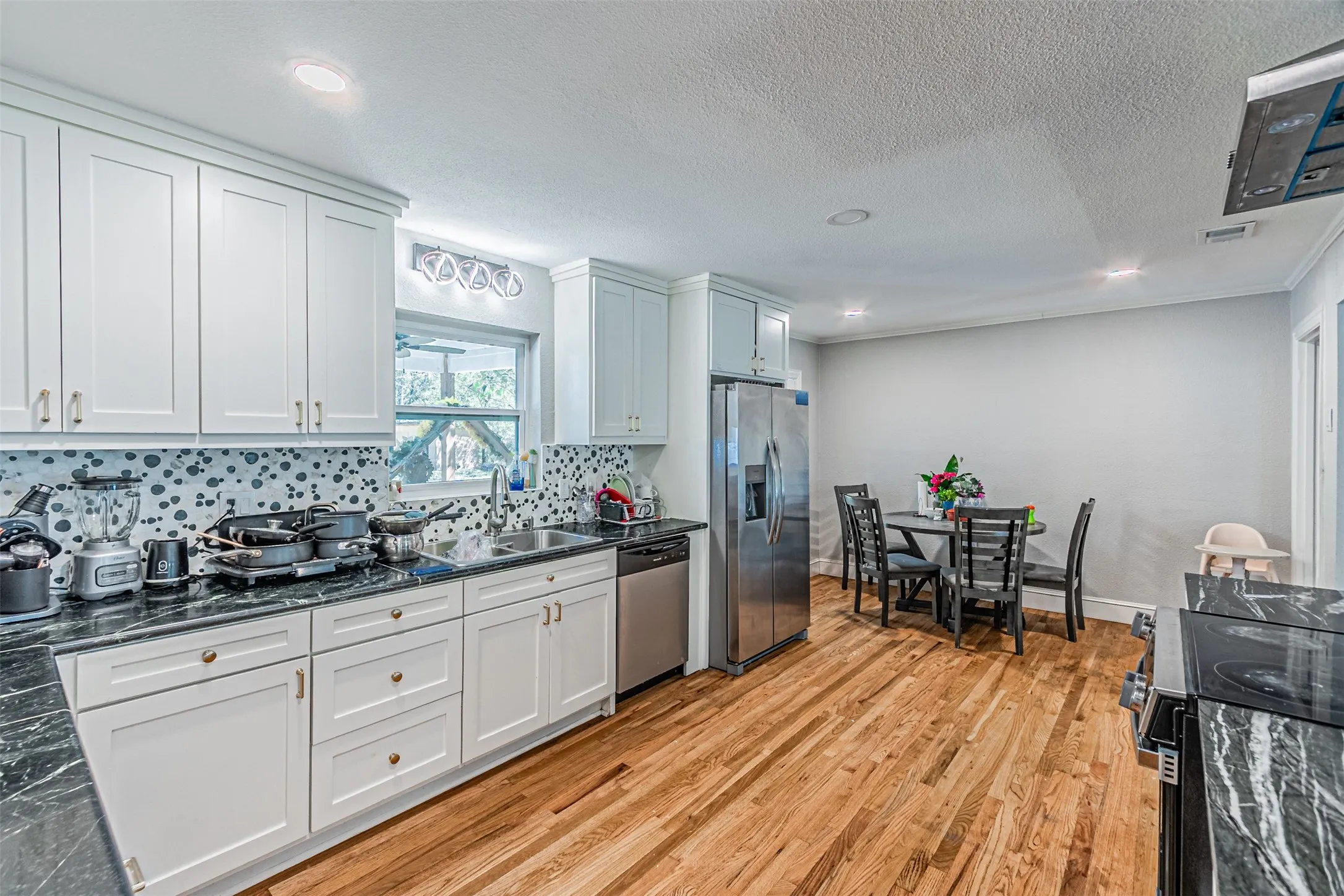 White shaker cabinetry, dark stone countertops, stainless steel appliances, wood-finish flooring, and a patterned tile backsplash