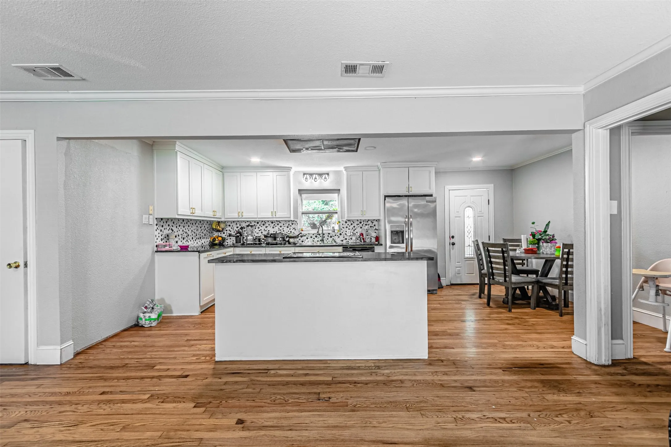 Wood-finish flooring throughout, white cabinetry, dark stone countertops, stainless steel appliances, and a mosaic tile backsplash