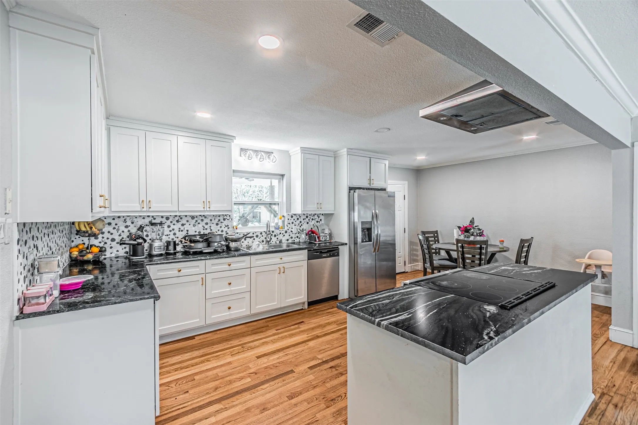 Kitchen featuring white cabinetry, dark stone countertops, stainless steel appliances, a patterned backsplash, and wood-finish flooring