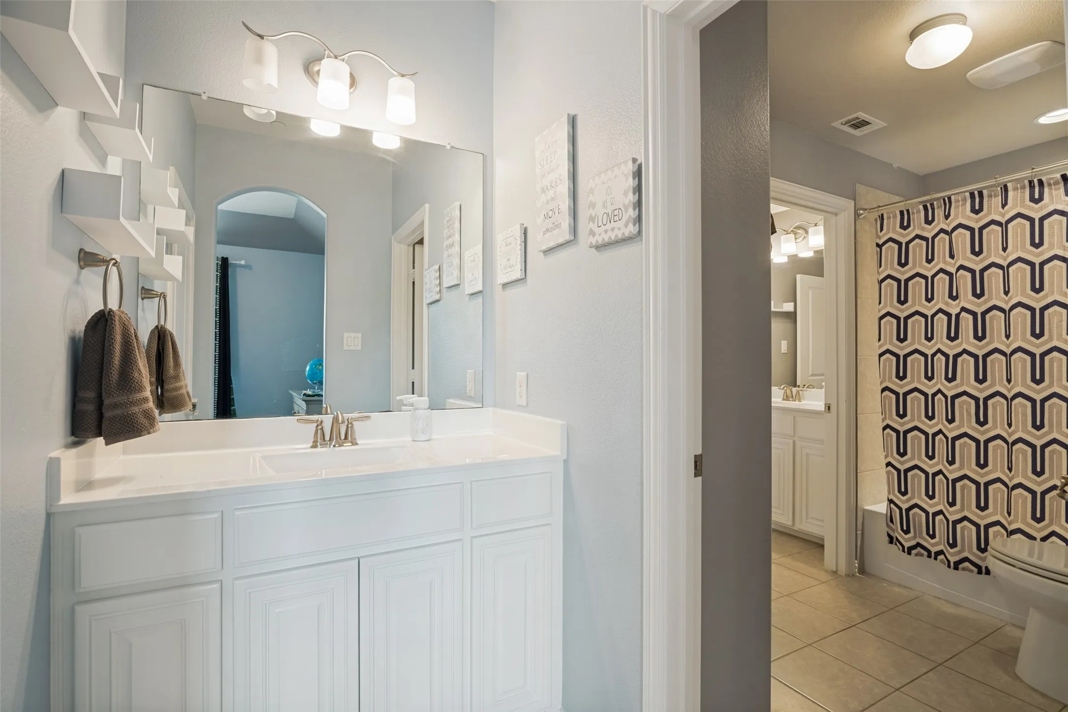 White vanity with integrated sink, expansive mirror, and a three-light fixture