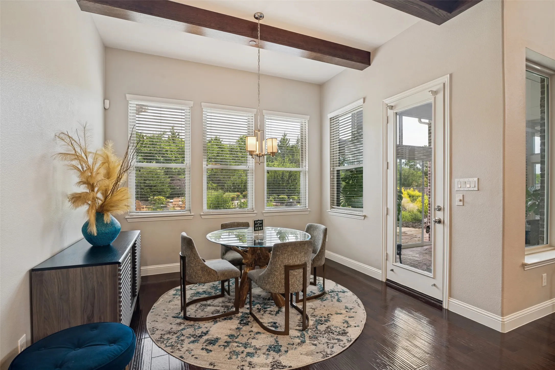 Wood-finish flooring, accent ceiling beams, multiple windows with blinds, a glass-paned door, and a built-in console