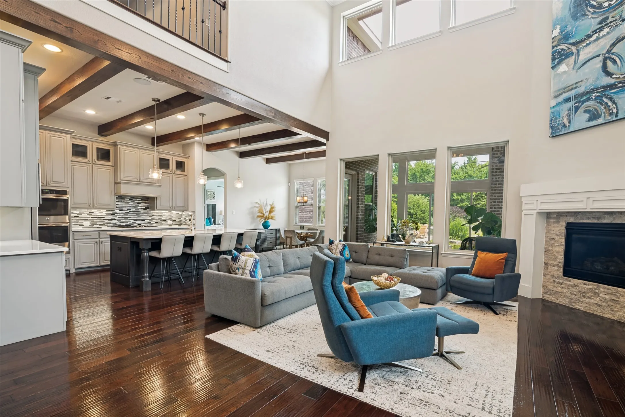 Two-story living area with exposed wood beams, wood-finish flooring, and a fireplace with stone surround