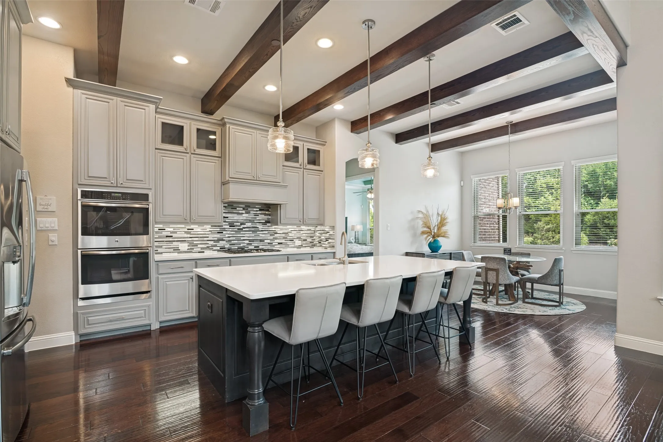Gourmet kitchen featuring a large central island, stainless steel double ovens, an integrated range hood, white shaker-style cabinetry, and wood-finish flooring