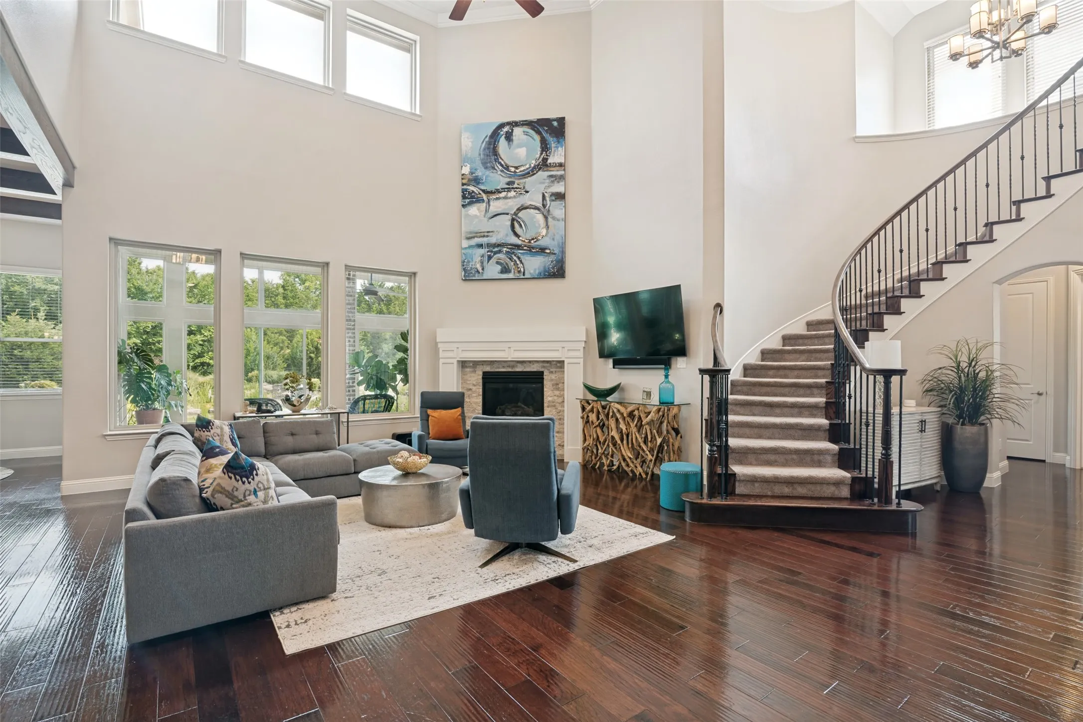 High ceilings with upper transom windows, dark wood-finish flooring, a curved staircase with metal balusters, and a fireplace with a mantel
