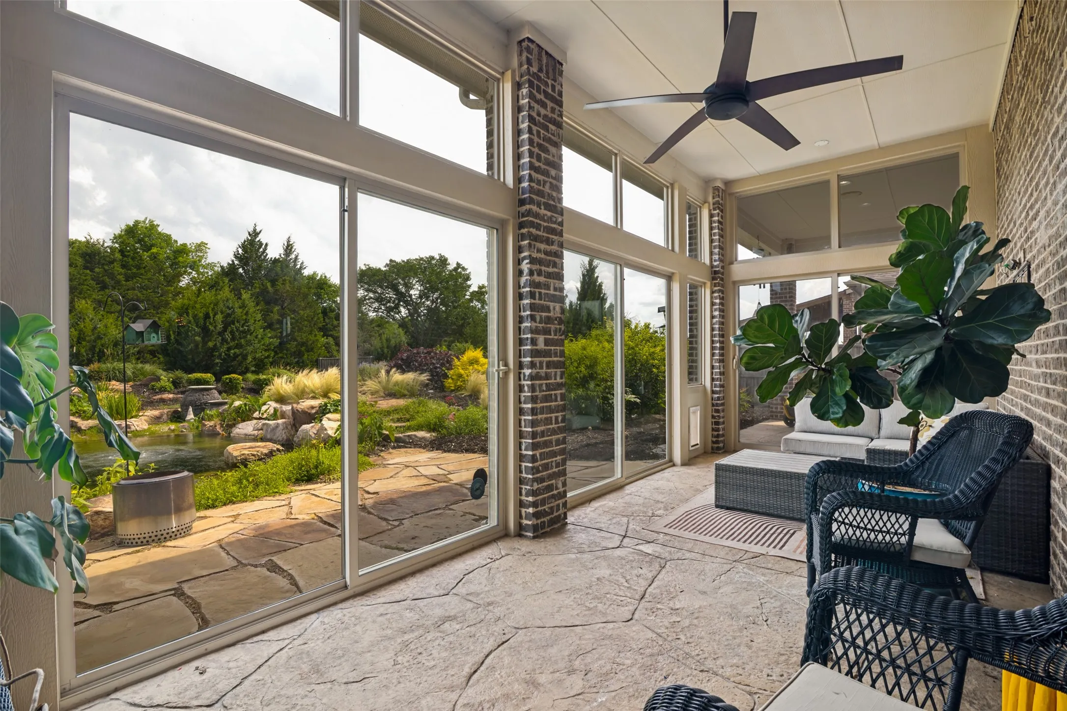 Enclosed patio with stamped concrete flooring, brick accent walls, and an overhead ceiling fan