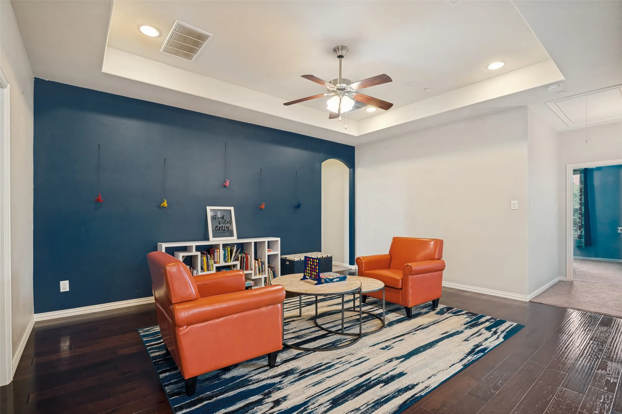 Tray ceiling with recessed lighting, ceiling fan, dark wood-finish flooring, and a built-in shelving unit