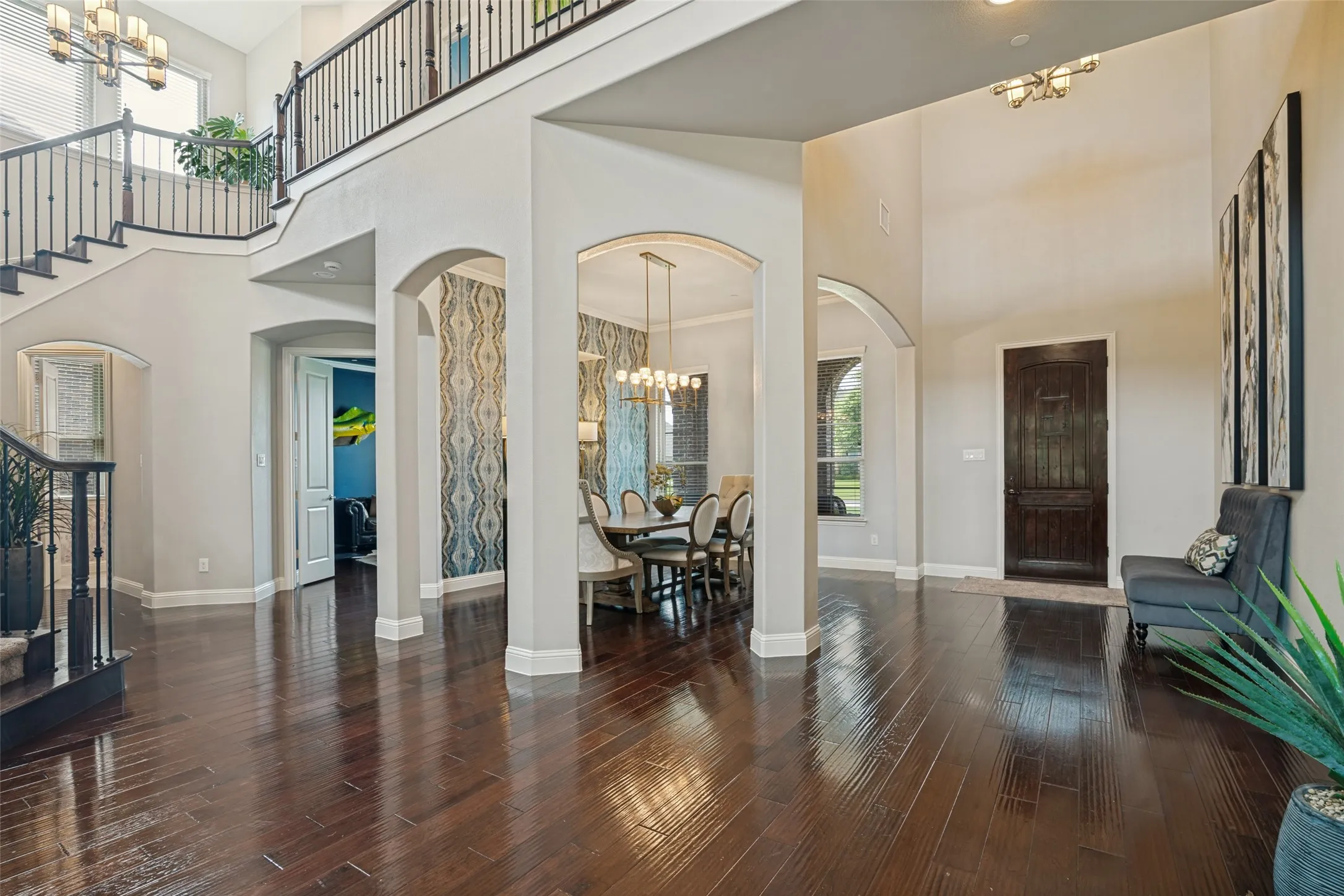 Two-story foyer featuring dark wood-finish flooring, a grand staircase with wrought iron balusters, arched entryways, and a double-height ceiling