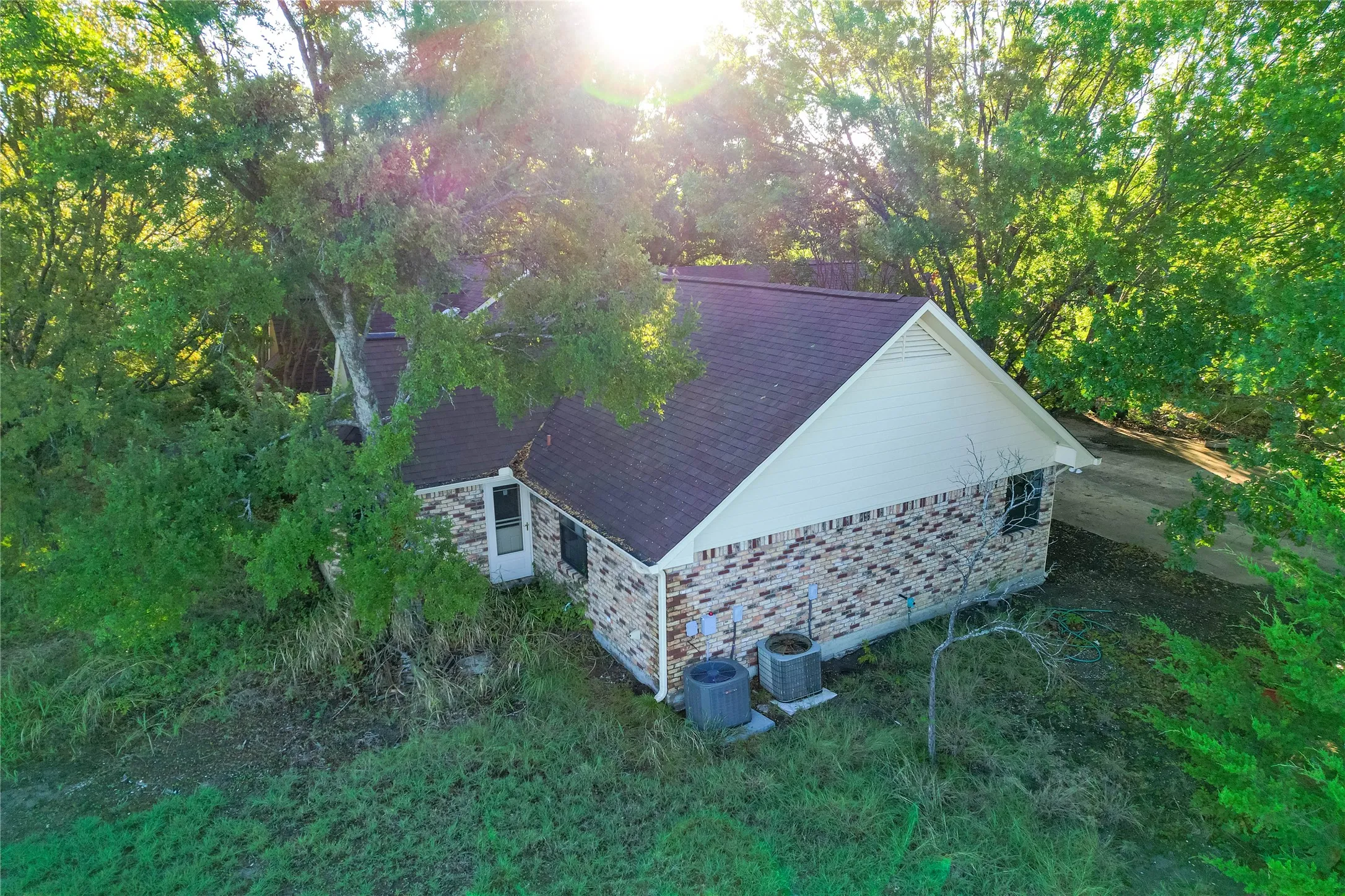 Brick exterior with a dark shingle roof, light-colored siding, and mature surrounding trees