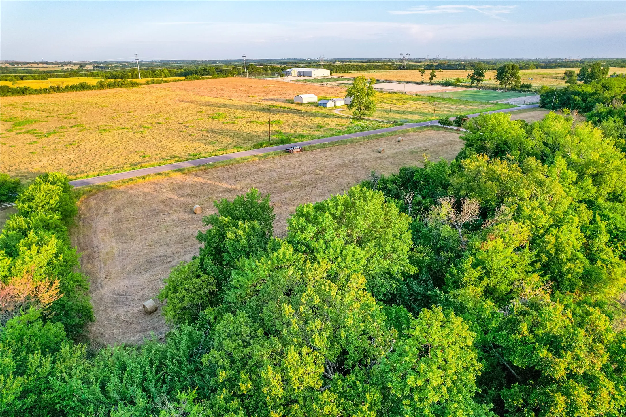 Expansive undeveloped land with a paved road, scattered mature trees, and agricultural fields