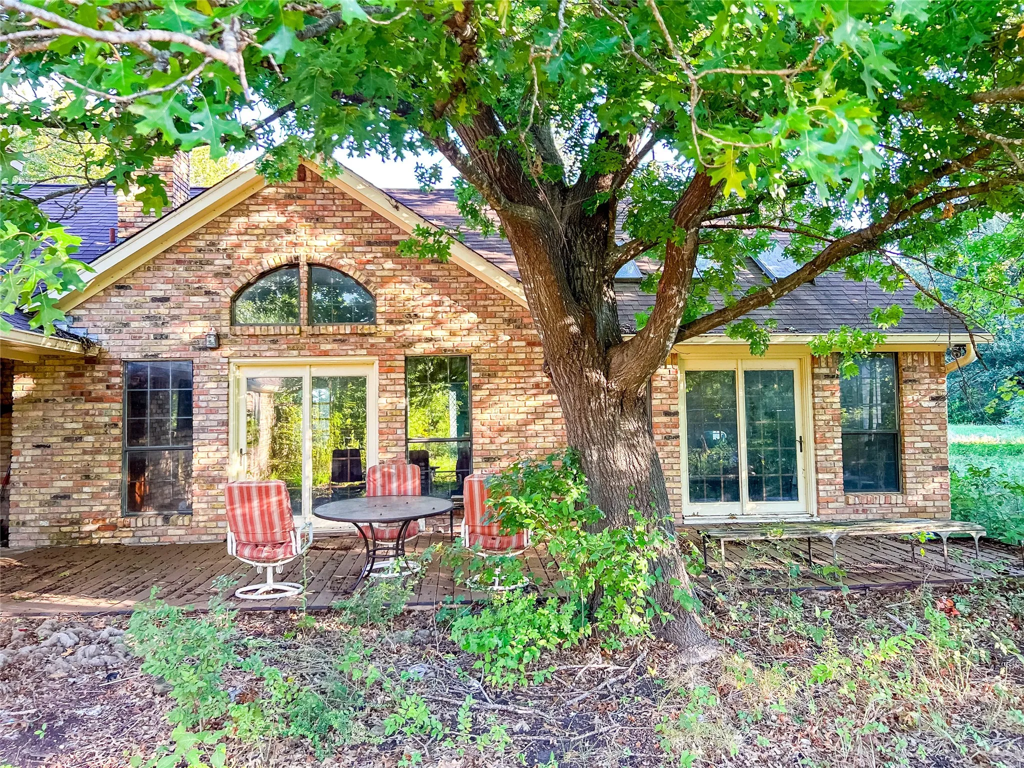 Brick exterior with a prominent arched window, multiple sliding glass doors, and a wood deck