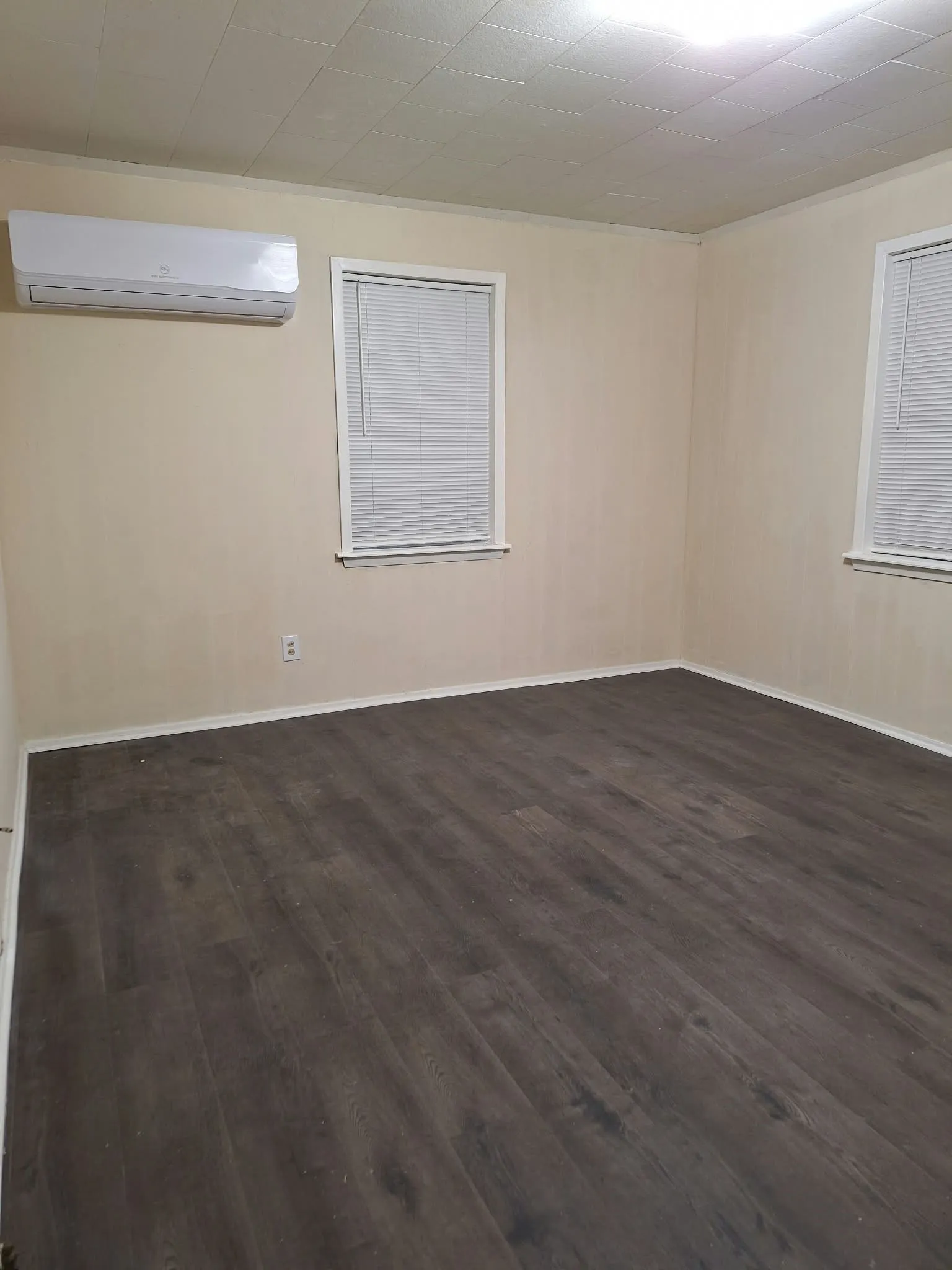 Wood-finish flooring, neutral wall tones, white trim, and a wall-mounted climate control unit