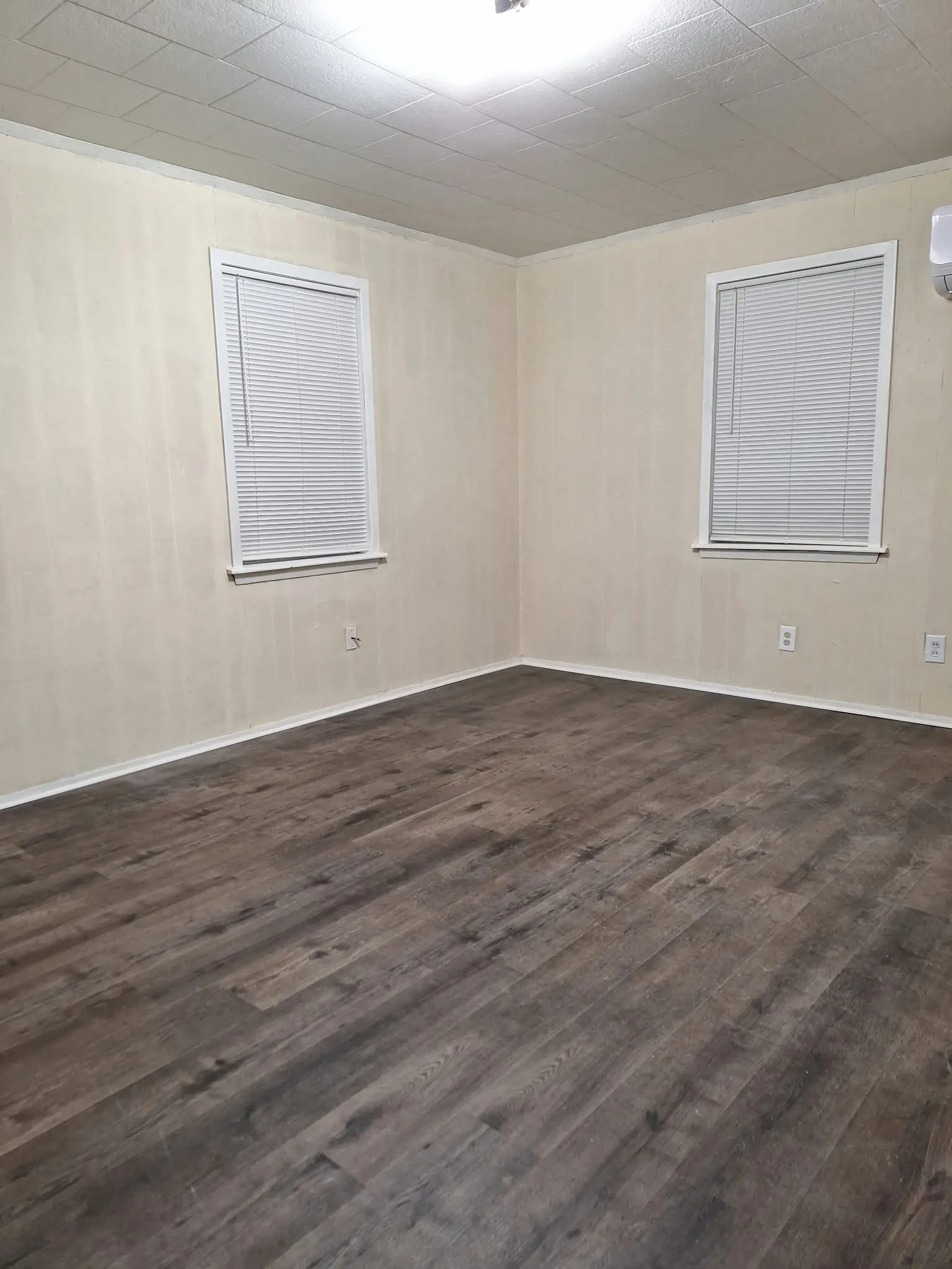 Wood-finish flooring with light-toned walls, featuring two windows with blinds, and white trim