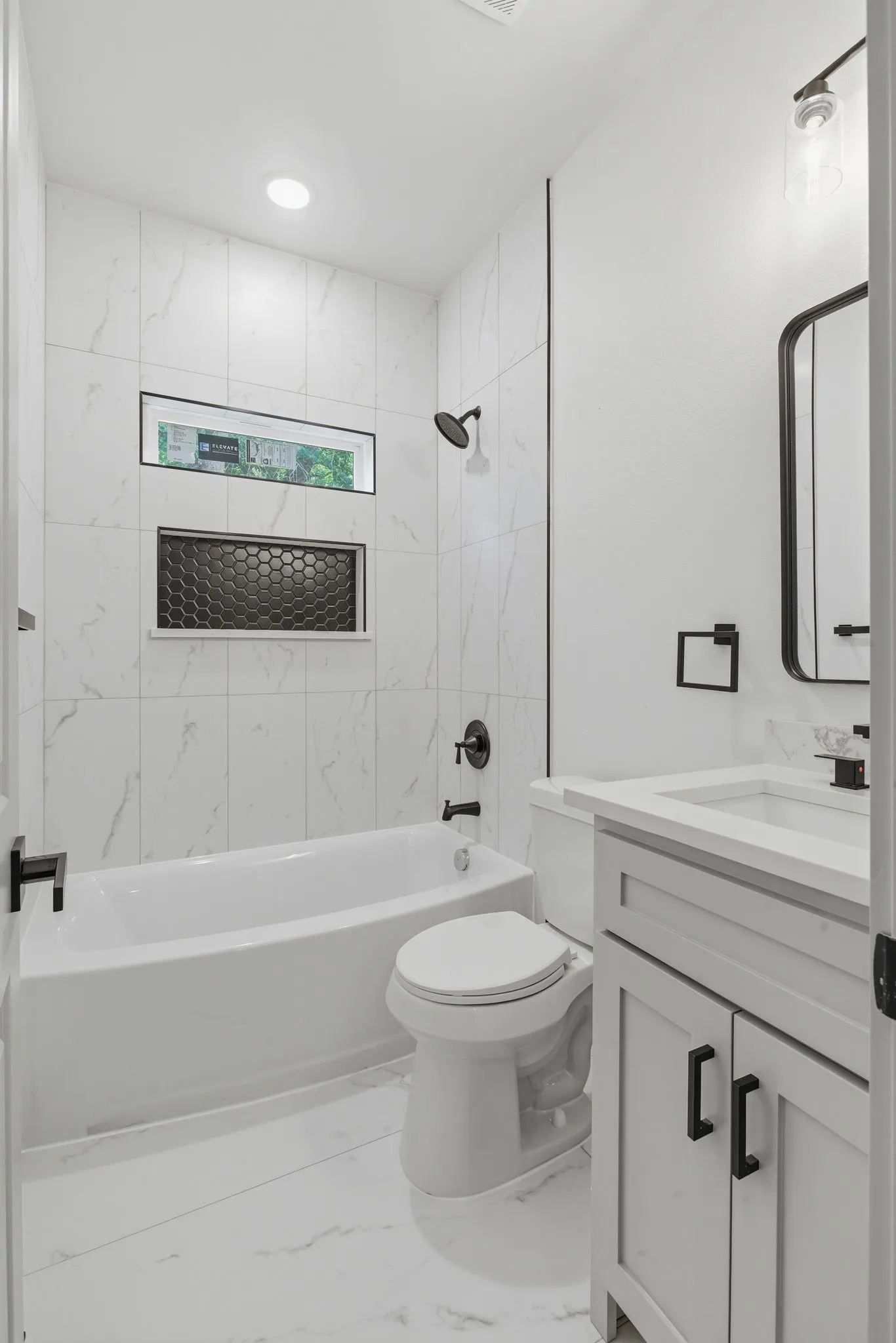 White tile flooring, white tile bath surround, built-in bathtub, built-in vanity with white countertop, and dark-finish fixtures